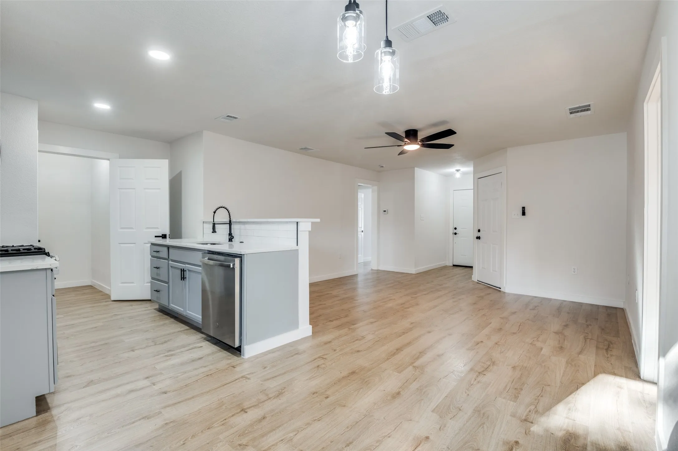 Kitchen with gray cabinets, light wood-style floors, open floor plan, stainless steel dishwasher, and decorative light fixtures
