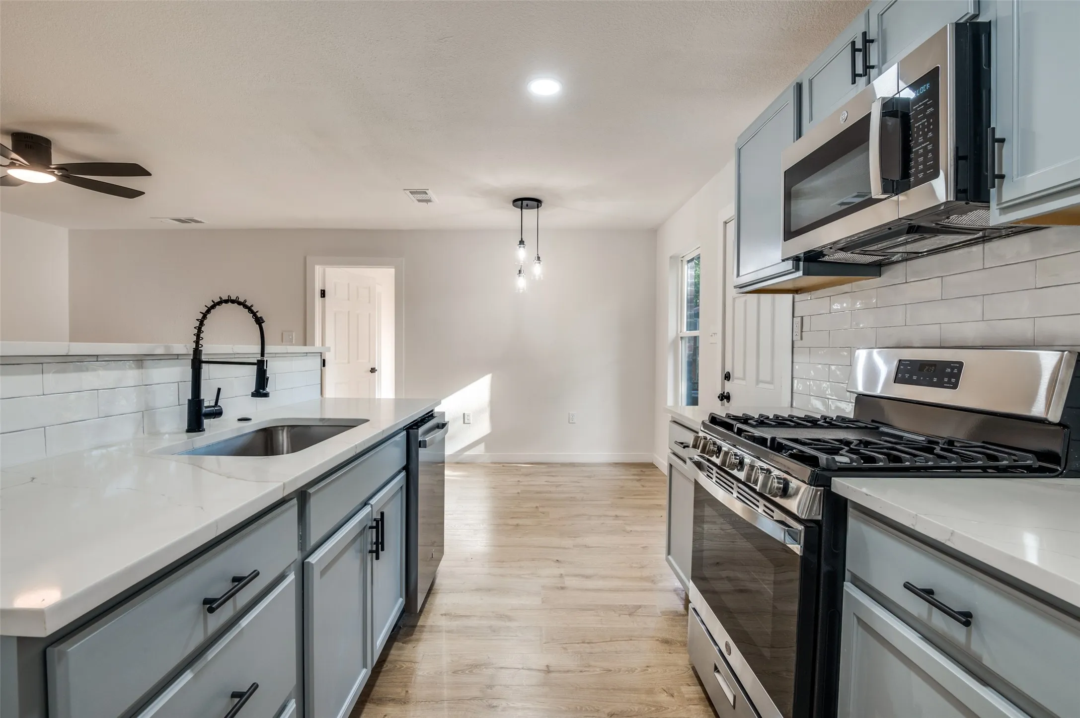Kitchen with tasteful backsplash, stainless steel appliances, gray cabinetry, pendant lighting, and light wood-type flooring