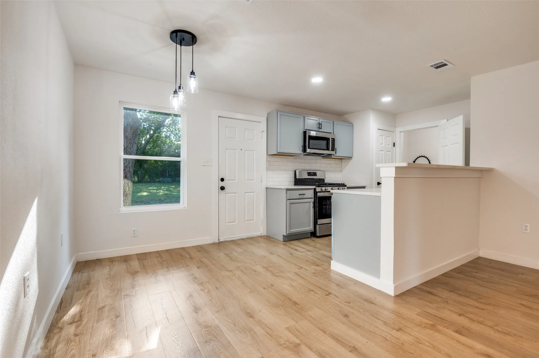 Kitchen with gray cabinetry, appliances with stainless steel finishes, light countertops, pendant lighting, and backsplash