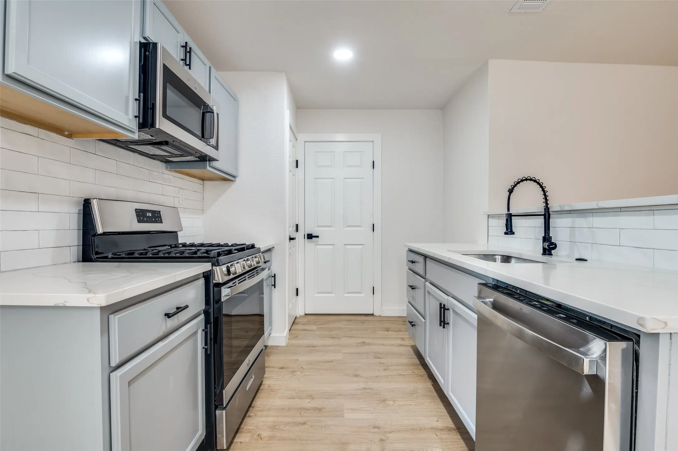 Kitchen with backsplash, stainless steel appliances, light stone countertops, light wood-style flooring, and recessed lighting