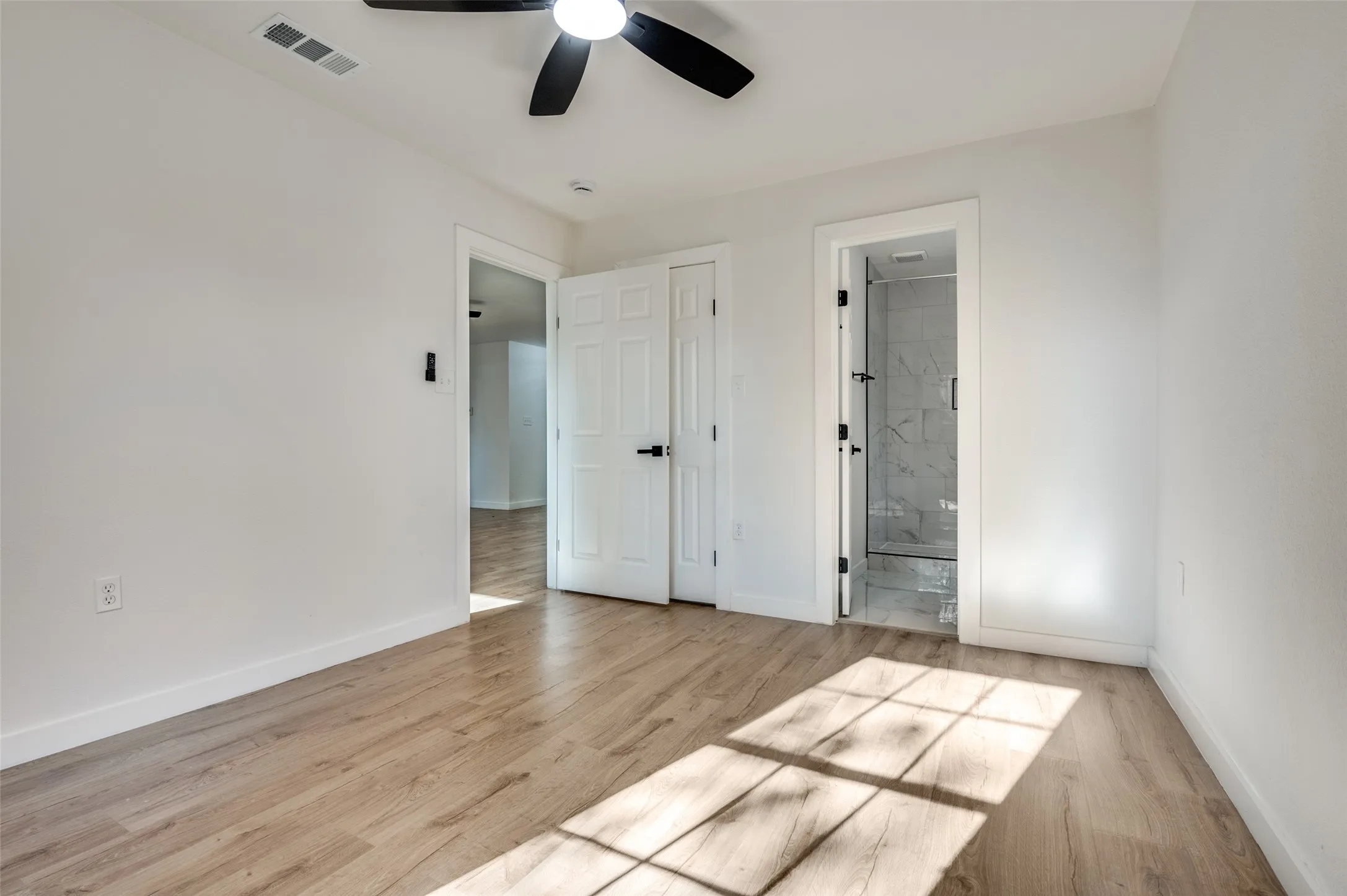 Unfurnished bedroom with light wood-style floors, a ceiling fan, and connected bathroom