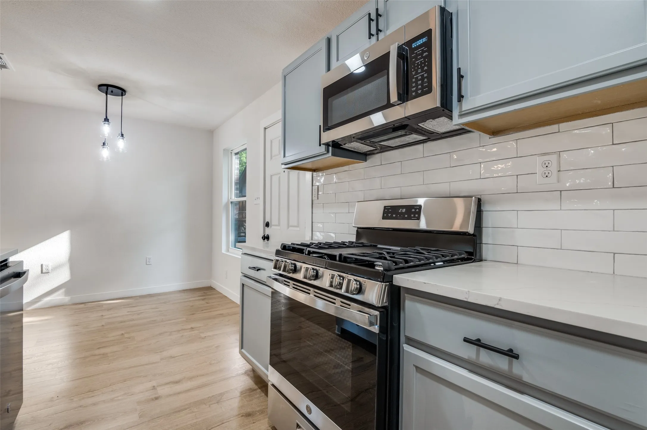 Kitchen with stainless steel appliances, decorative light fixtures, decorative backsplash, light stone countertops, and light wood finished floors