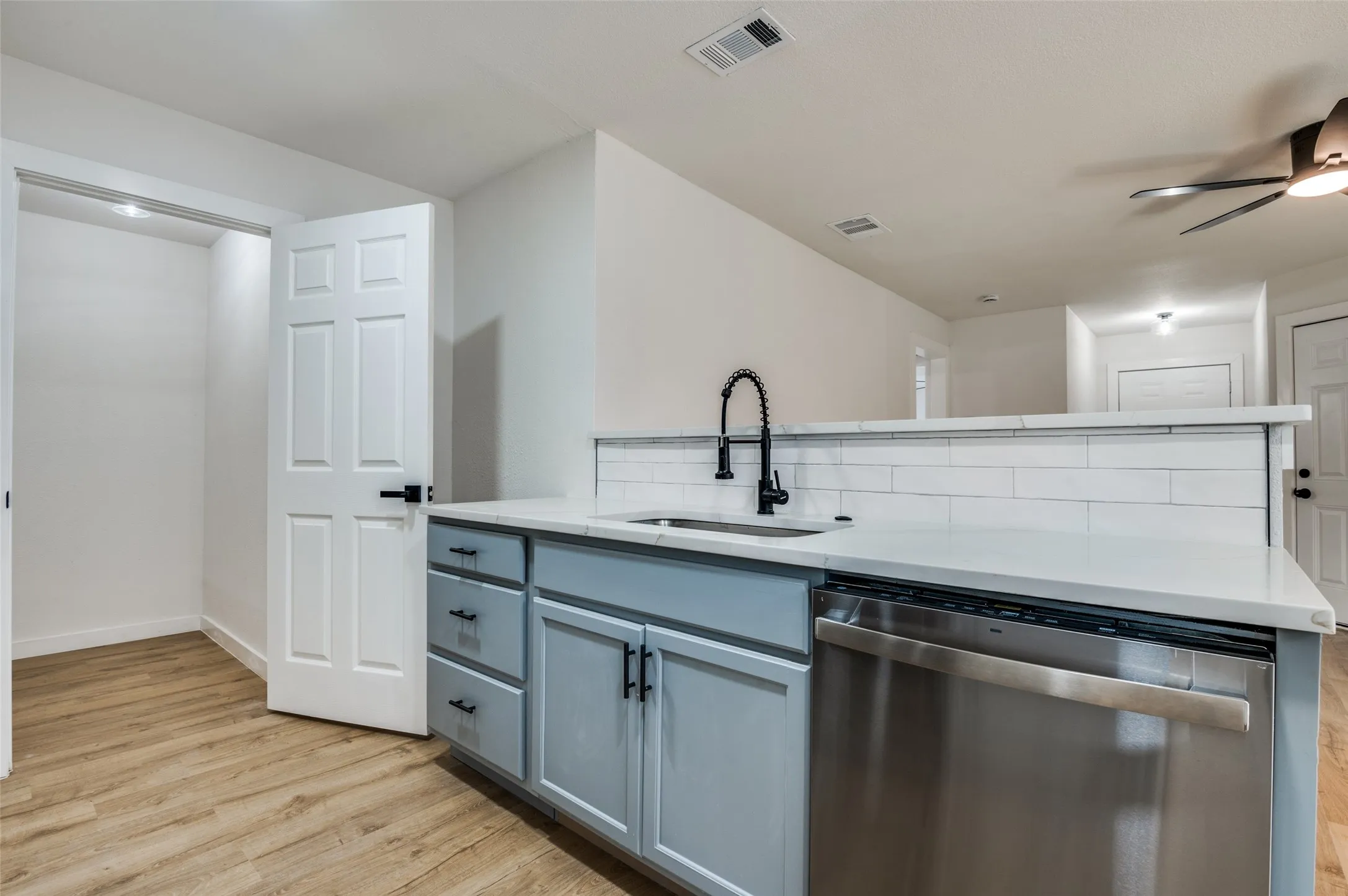 Kitchen featuring dishwasher, light stone countertops, light wood-style flooring, backsplash, and a ceiling fan
