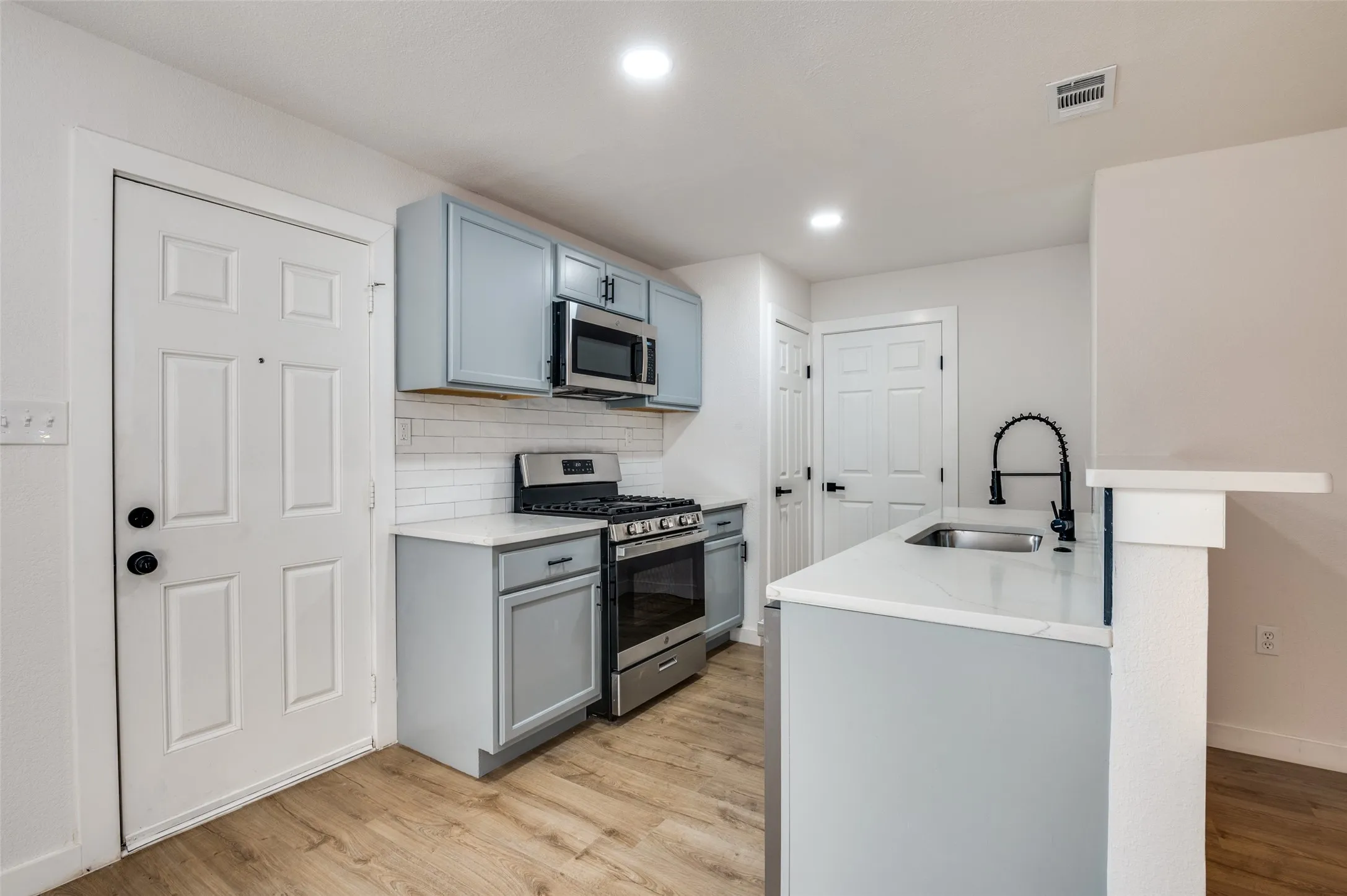 Kitchen featuring tasteful backsplash, appliances with stainless steel finishes, light wood finished floors, recessed lighting, and gray cabinetry