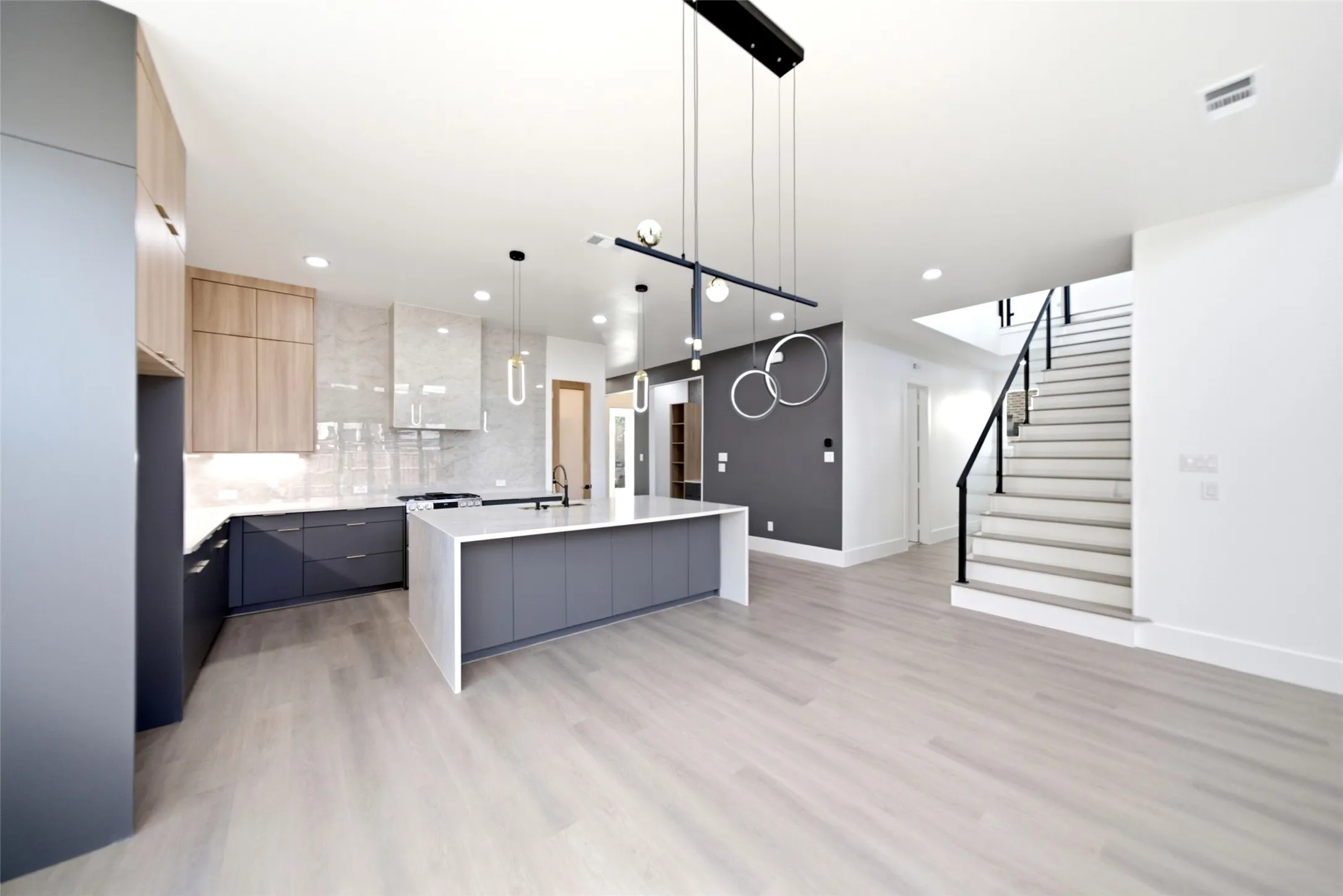 Modern kitchen featuring a large island, wood-finish flooring, recessed lighting, and a contemporary staircase with dark railings