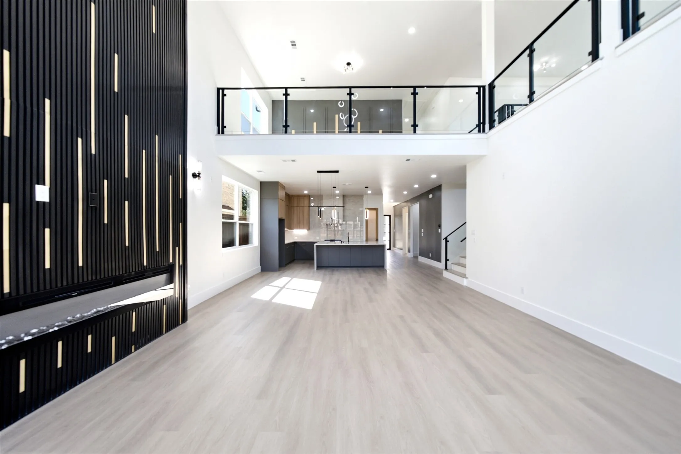 Open-concept living space with light wood-finish flooring, a two-story ceiling, and a modern fireplace