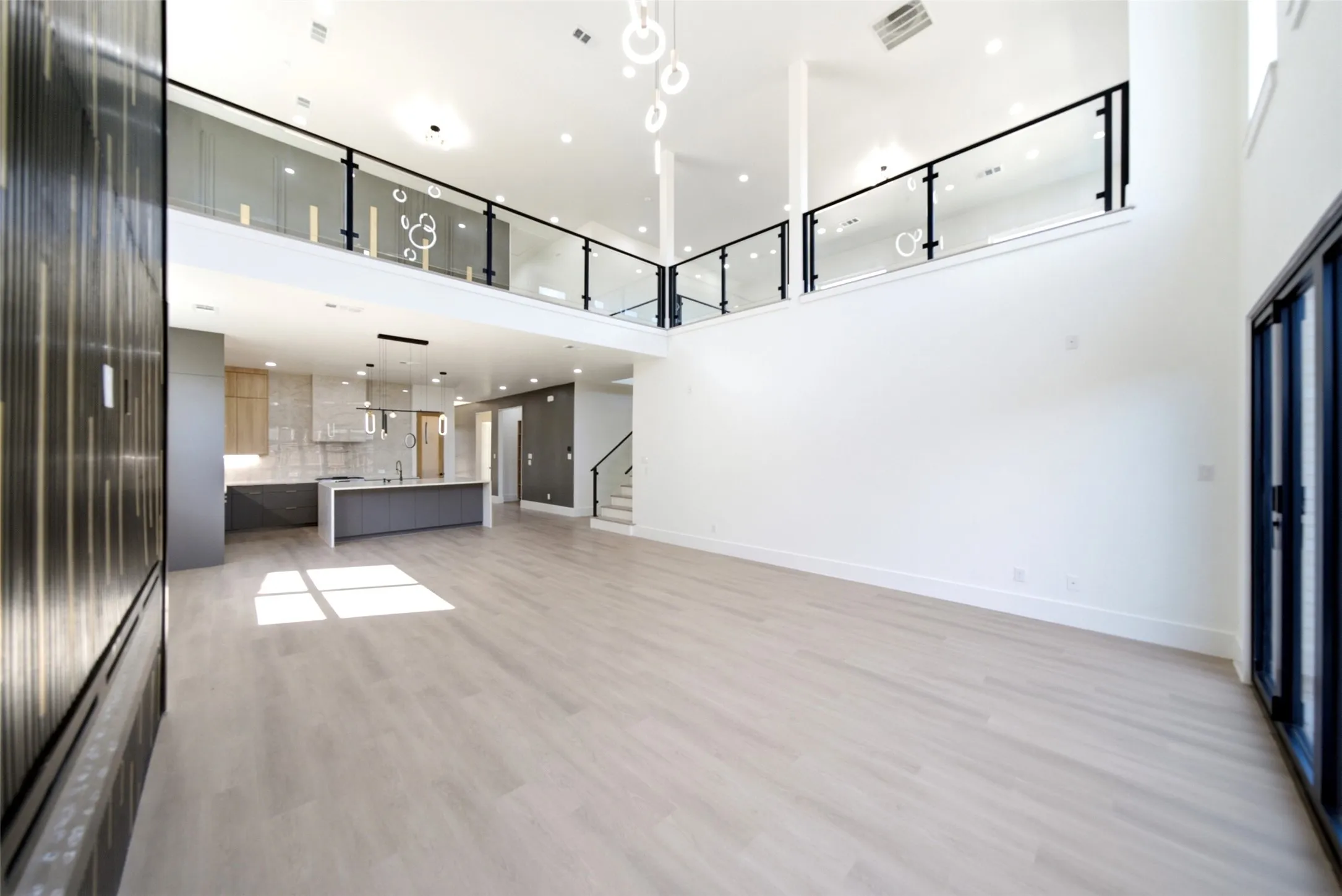 Vaulted ceilings, a contemporary open-concept kitchen, light wood-finish flooring, a glass and metal railing, and an expansive wall space
