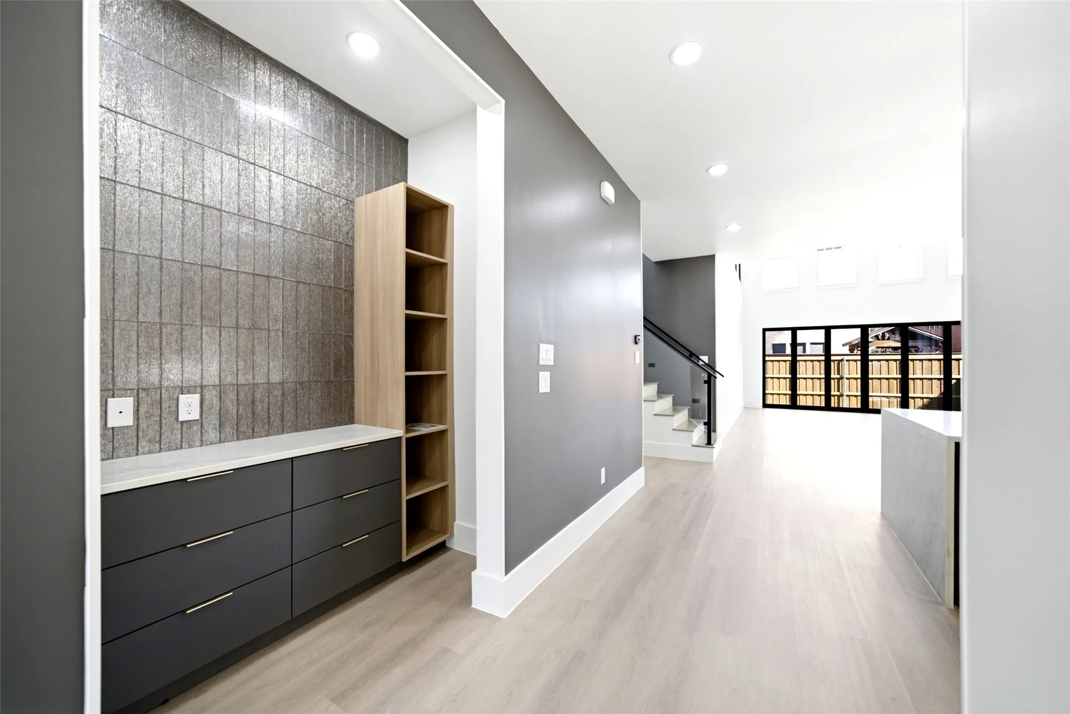 Built-in cabinetry with ample storage, textured accent wall, light wood-finish flooring, recessed lighting, and a contemporary staircase with dark railing