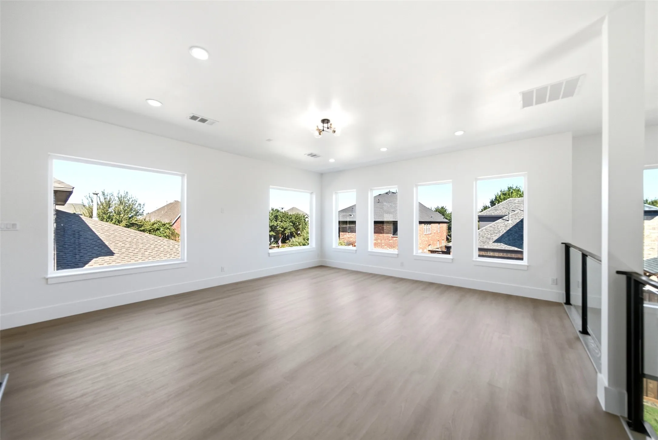 Spacious room with light wood-finish flooring, multiple windows, recessed ceiling lights, and a modern chandelier