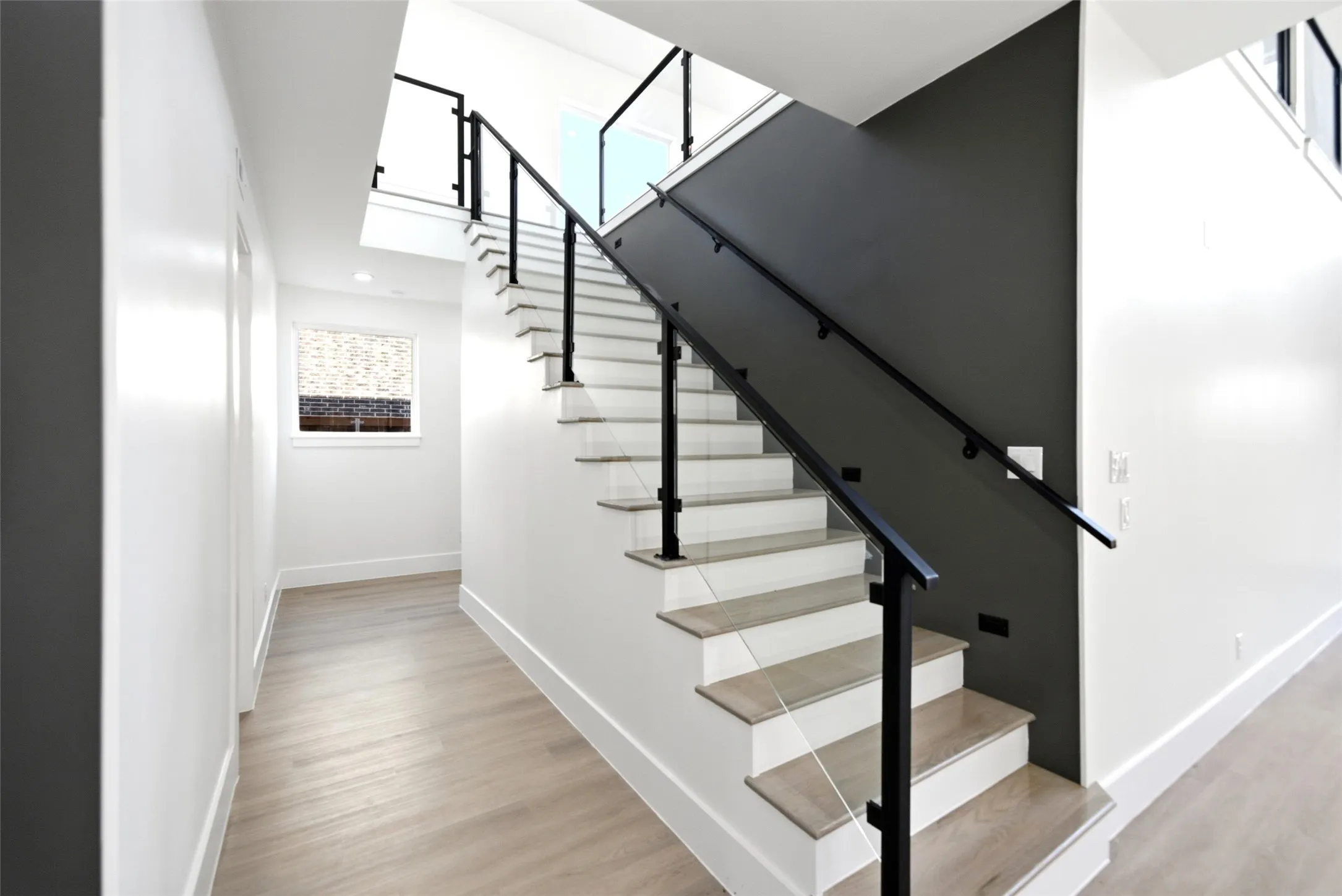 Modern staircase with black metal railings, light-toned wood-finish treads, and white risers