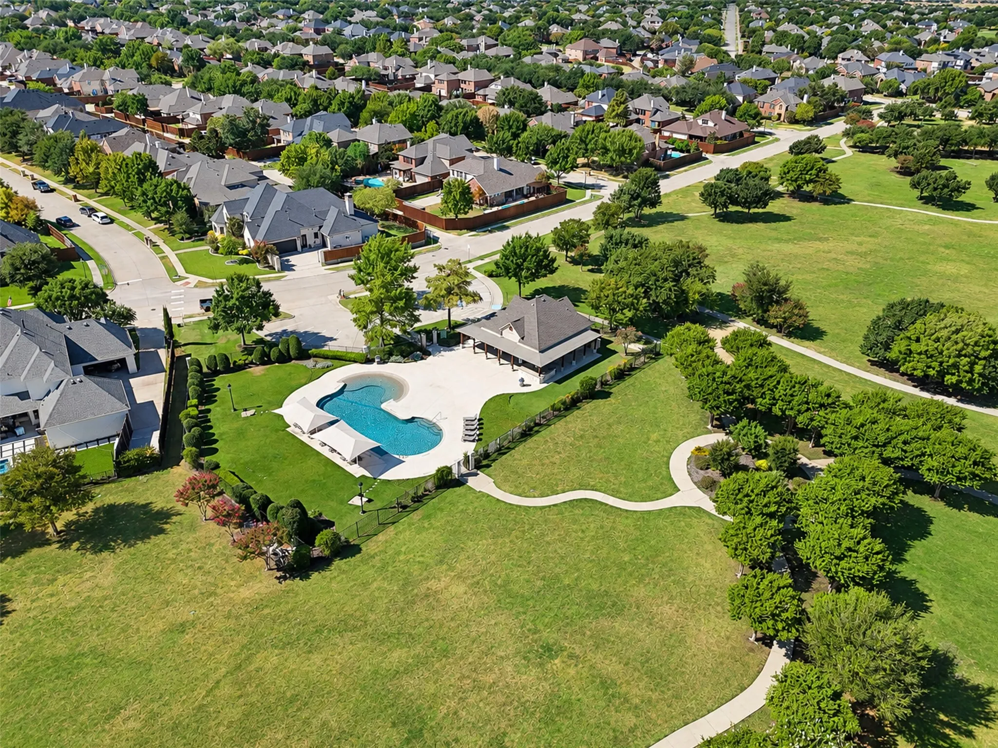 Community amenities featuring a swimming pool, covered outdoor seating, a paved pathway, and extensive green spaces