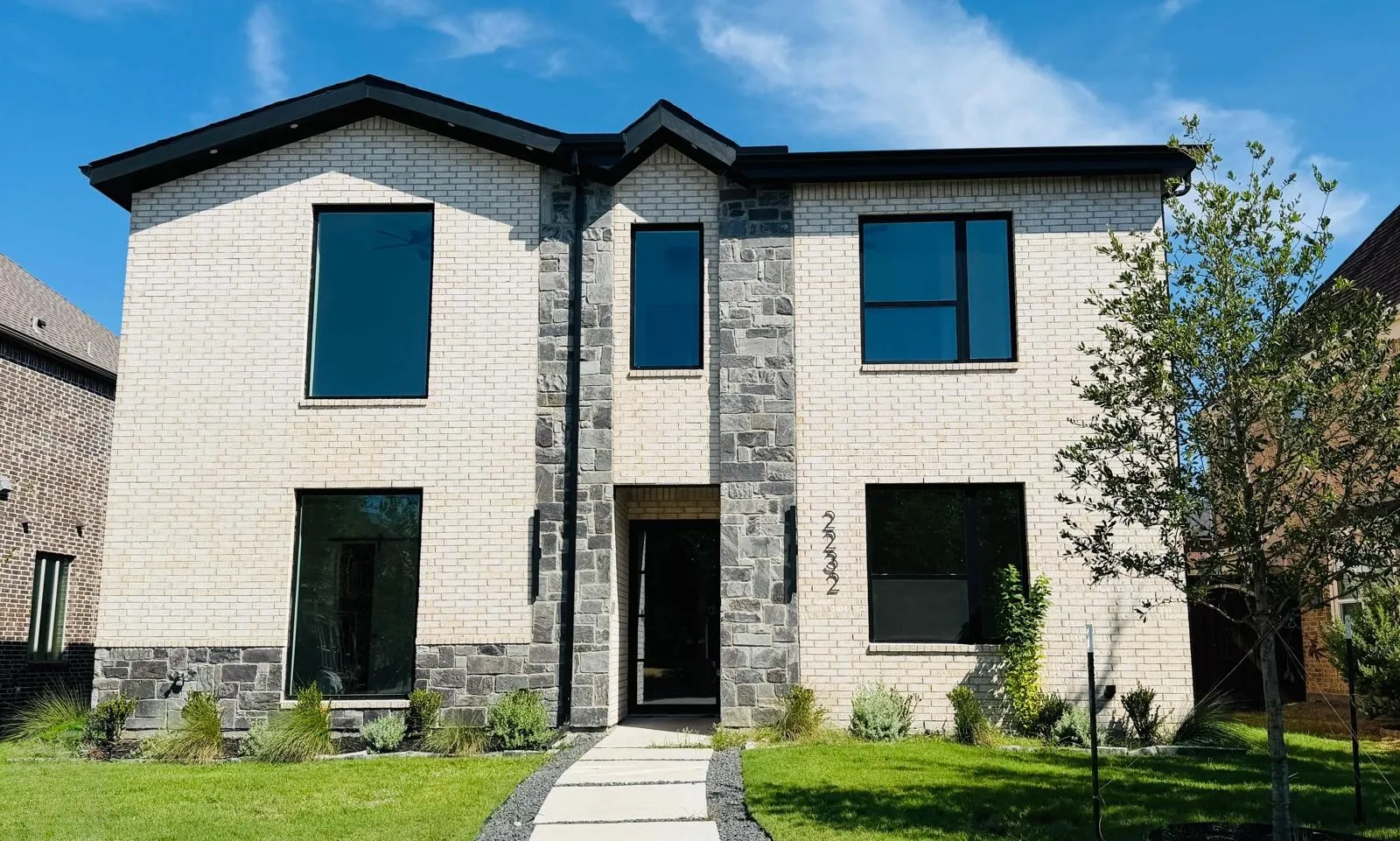 Contemporary facade featuring light-colored brick, dark stone accents, and black-framed windows