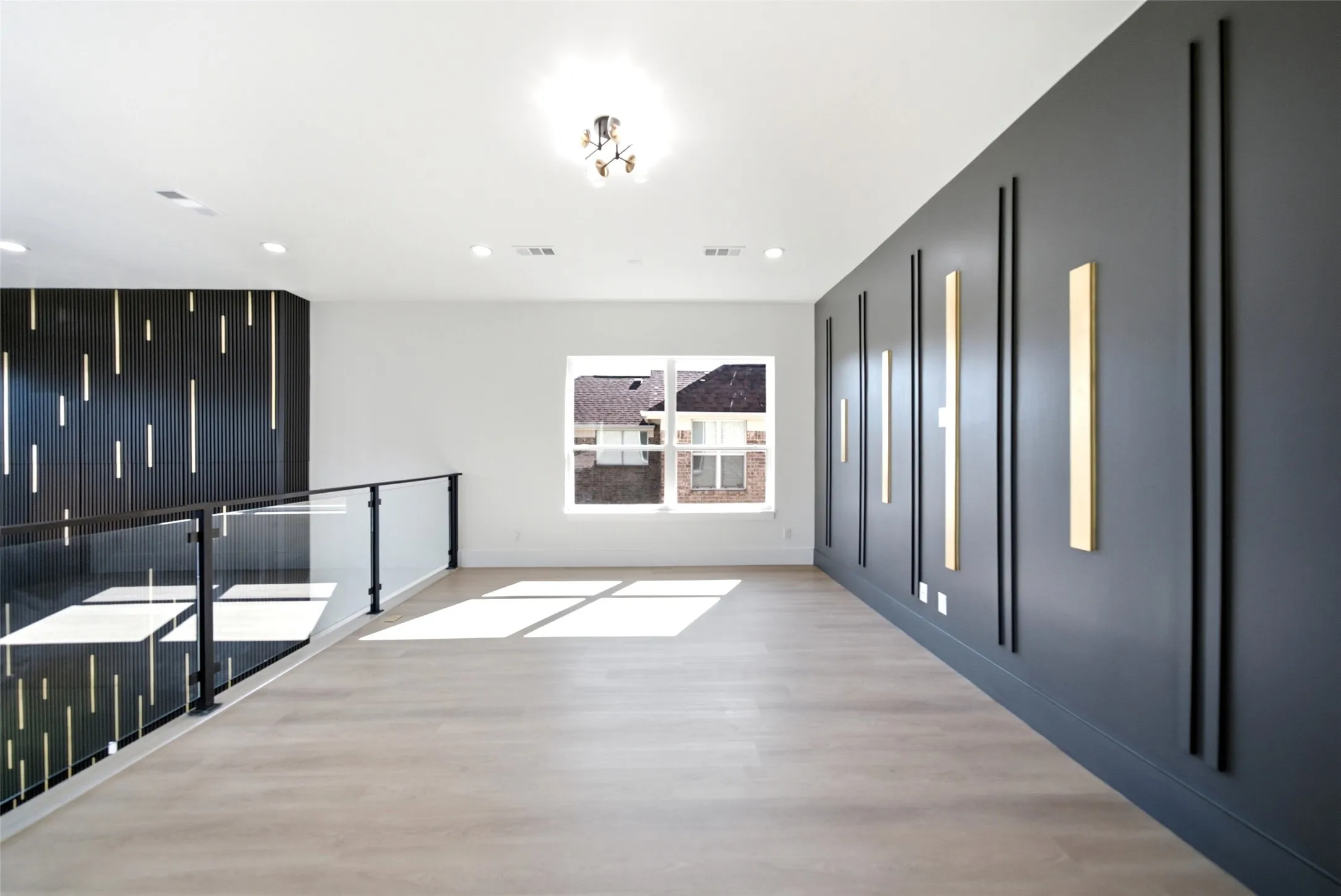 Open concept space featuring light wood-finish flooring, a contemporary chandelier, a built-in dark wood accent wall with vertical lighting, and a dark gray accent wall with vertical sconces
