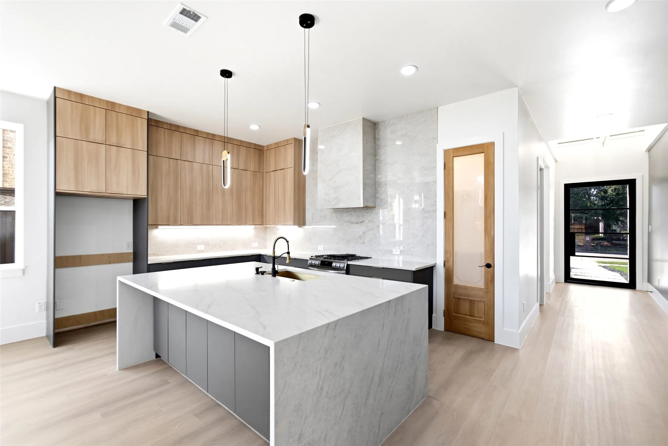 Kitchen featuring a waterfall island, wood-finish cabinetry, a built-in range, a matching range hood, and pendant lighting