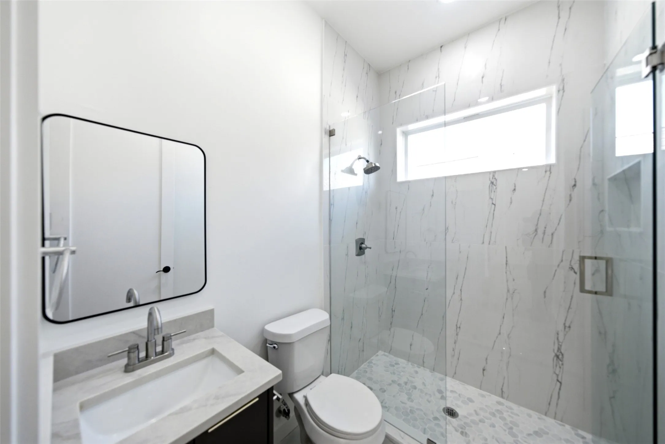 Vanity with a rectangular sink, a framed mirror, and a glass-enclosed shower with a transom window