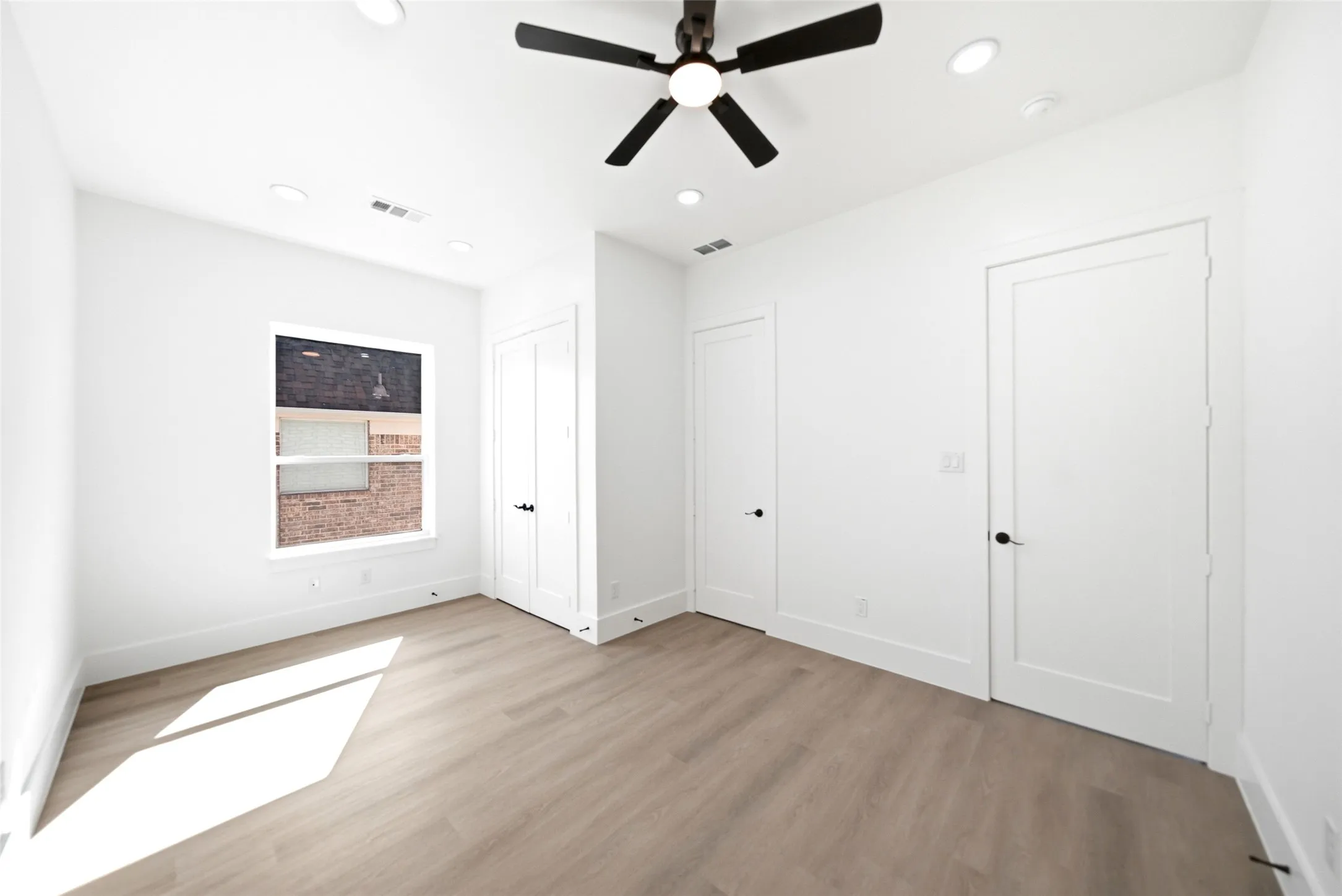 Recessed lighting, wood-finish flooring, ceiling fan, white paneled doors with black hardware, and a window