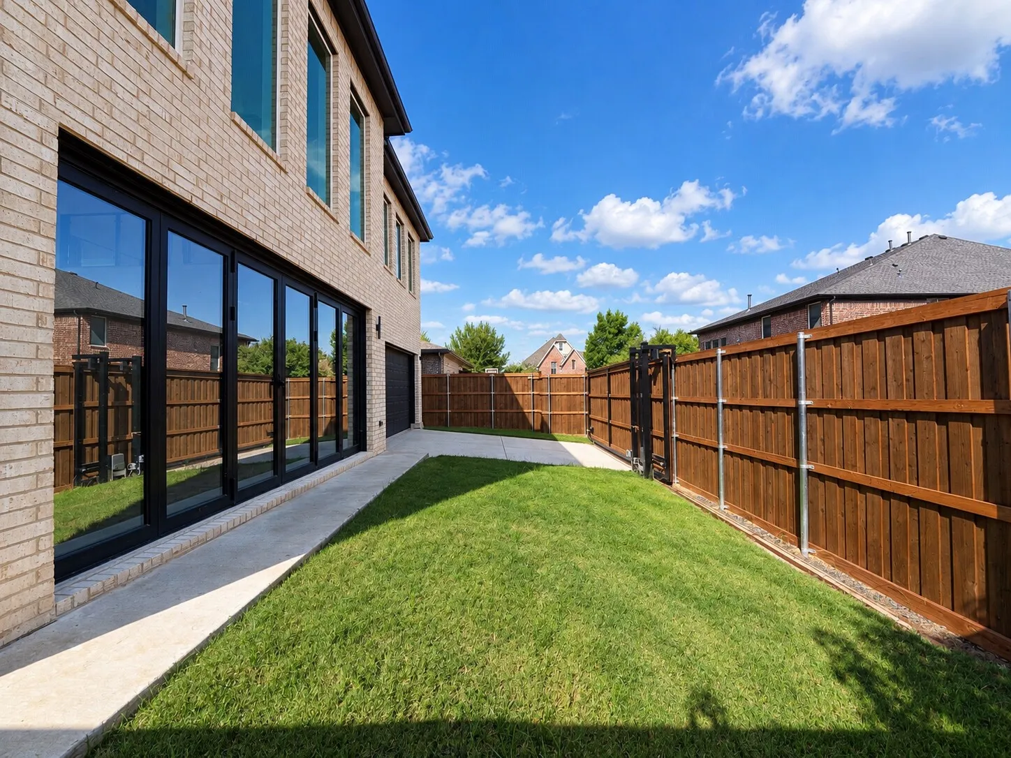 Brick exterior with multi-panel sliding glass doors, a concrete patio, a manicured lawn, and a privacy fence