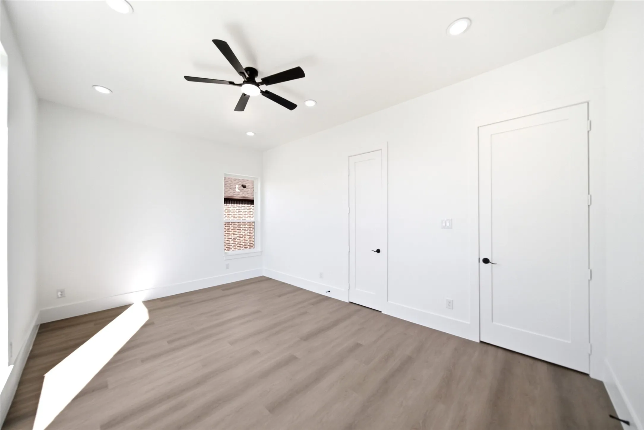 Recessed ceiling lighting, wood-finish flooring, white walls, black ceiling fan, and two interior doors