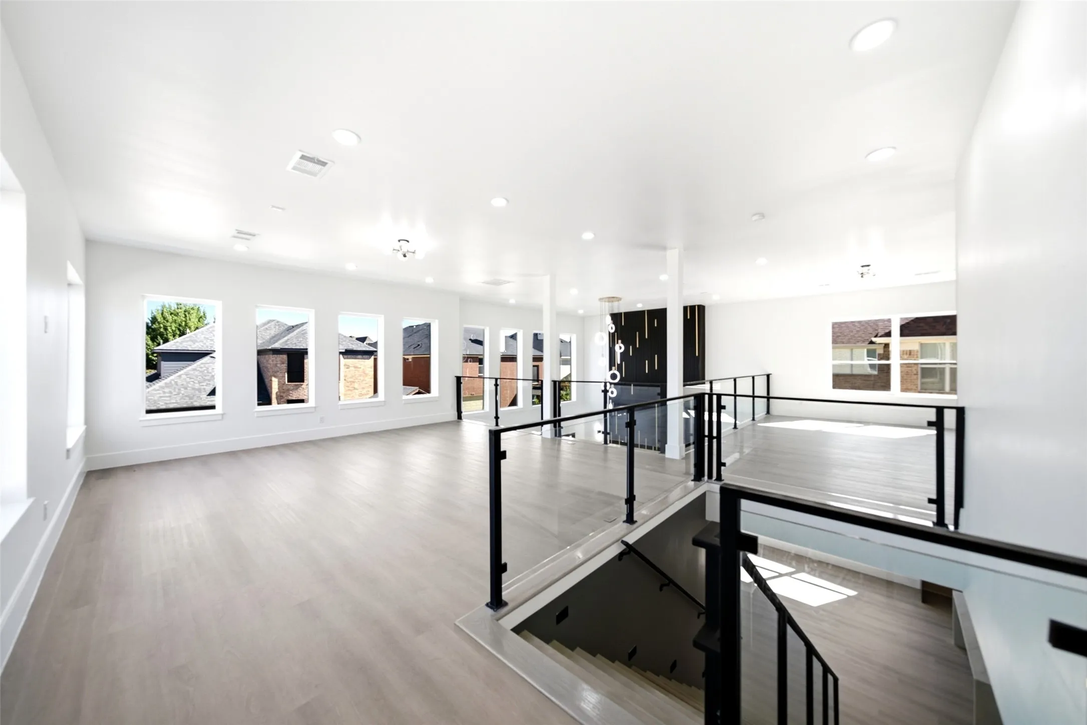 Expansive open-concept space featuring wood-finish flooring, numerous windows, recessed lighting, and a contemporary staircase with glass and metal railings