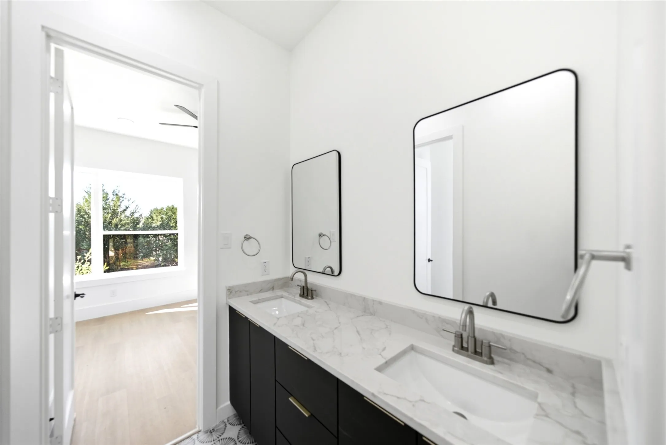 Spa-inspired primary bathroom featuring a marble-topped dual-sink vanity, matte black hardware, and framed mirrors with rounded corners