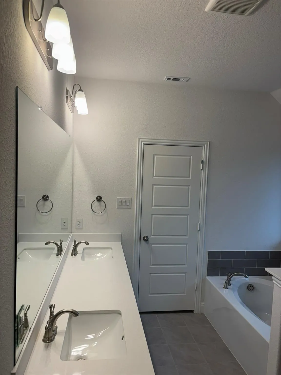 Dual vanity with integrated sinks, white countertops, brushed nickel faucets, and a built-in bathtub with subway tile surround