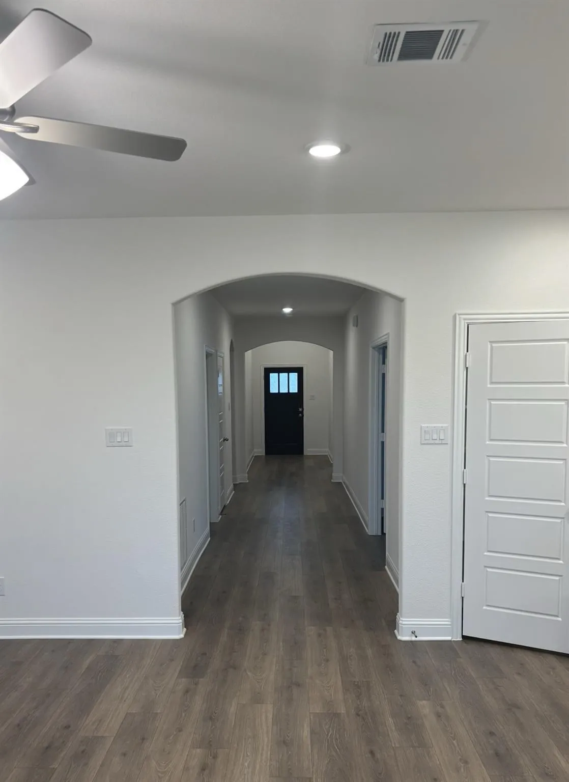 Wood-finish flooring throughout, complemented by a hallway archway, recessed lighting, and a ceiling fan