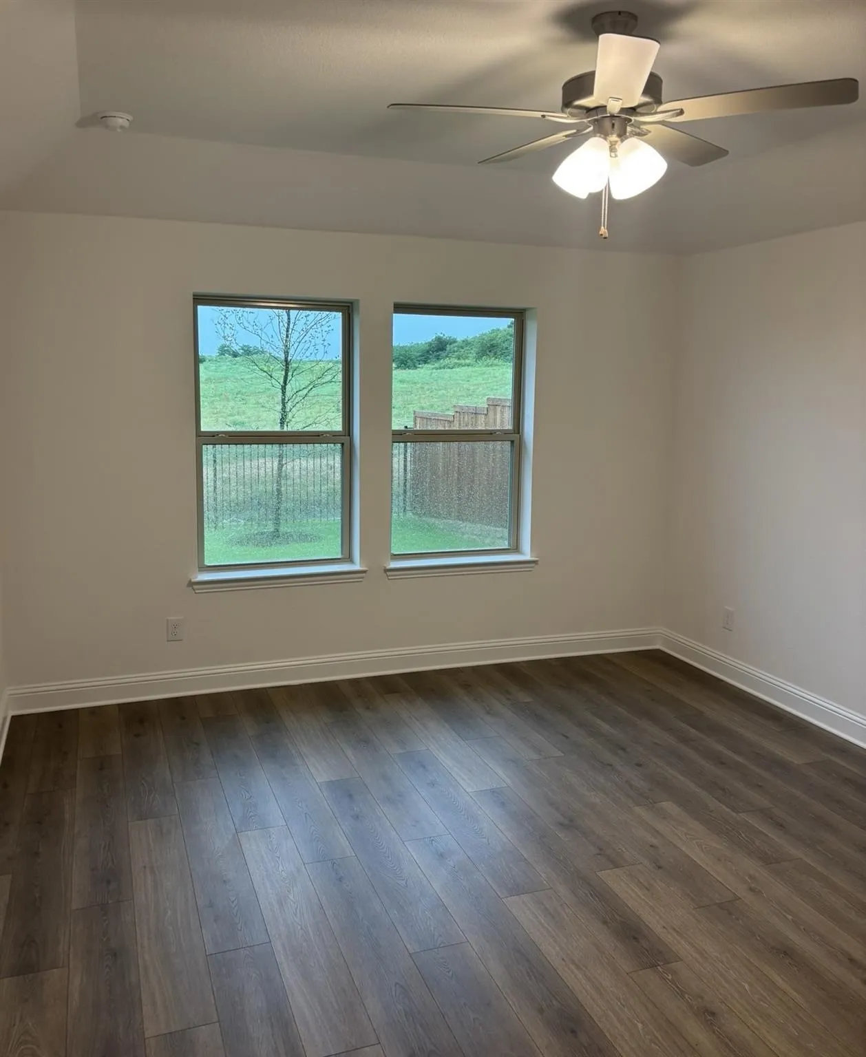 Wood-finish flooring, dual windows, and a ceiling fan with integrated lighting
