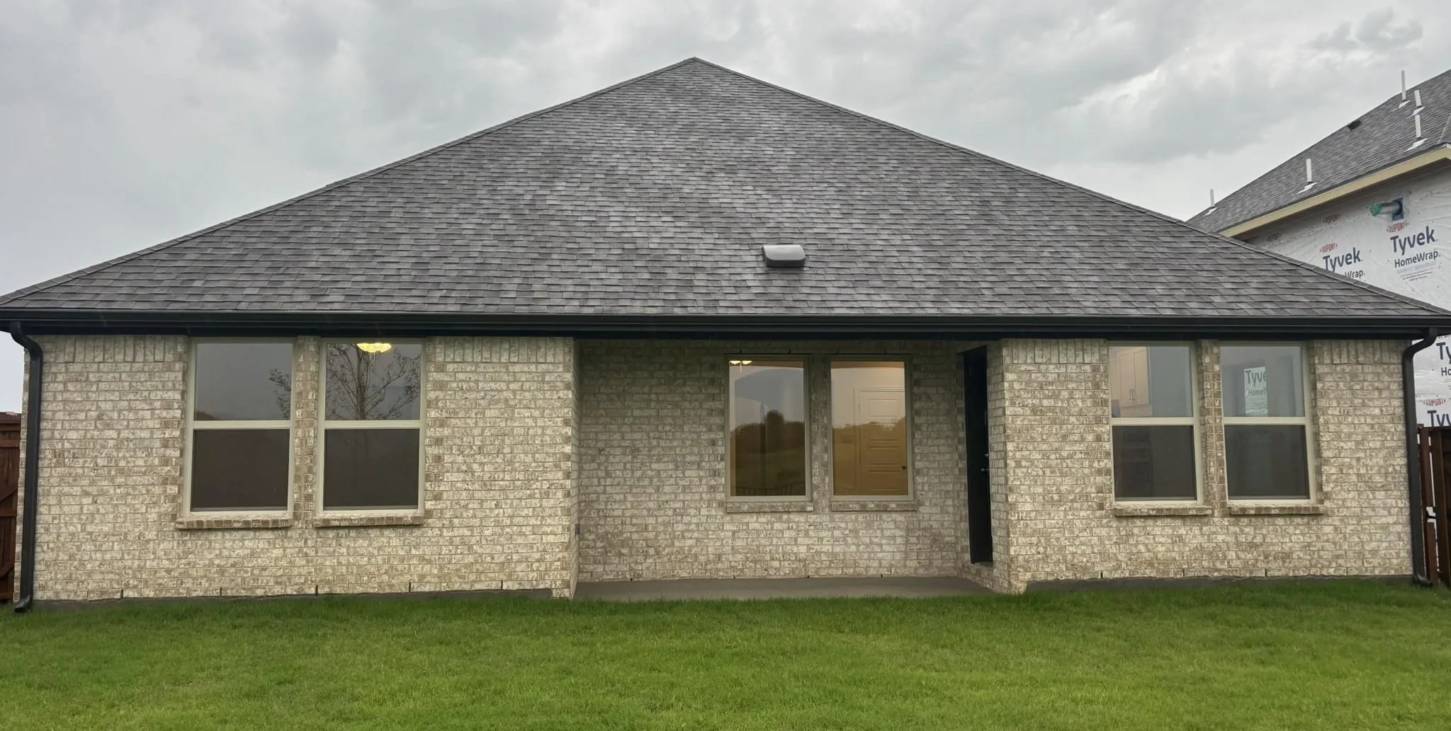 Brick exterior with a covered patio, multiple windows, and a shingle roof