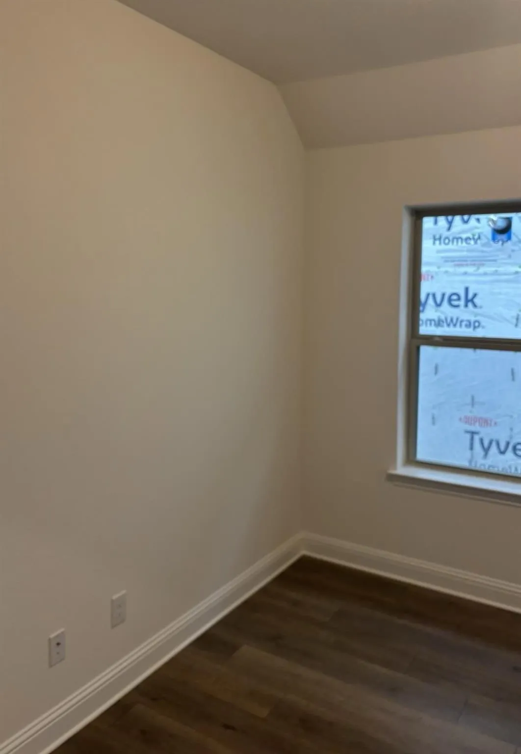 Wood-finish flooring with white baseboards, a window with white trim, and light-colored walls