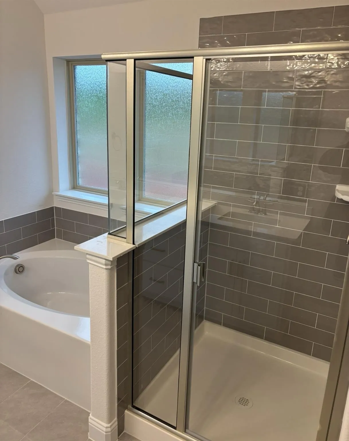 Deep soaking tub, glass-enclosed shower, subway tile surround, frosted window, and tile flooring
