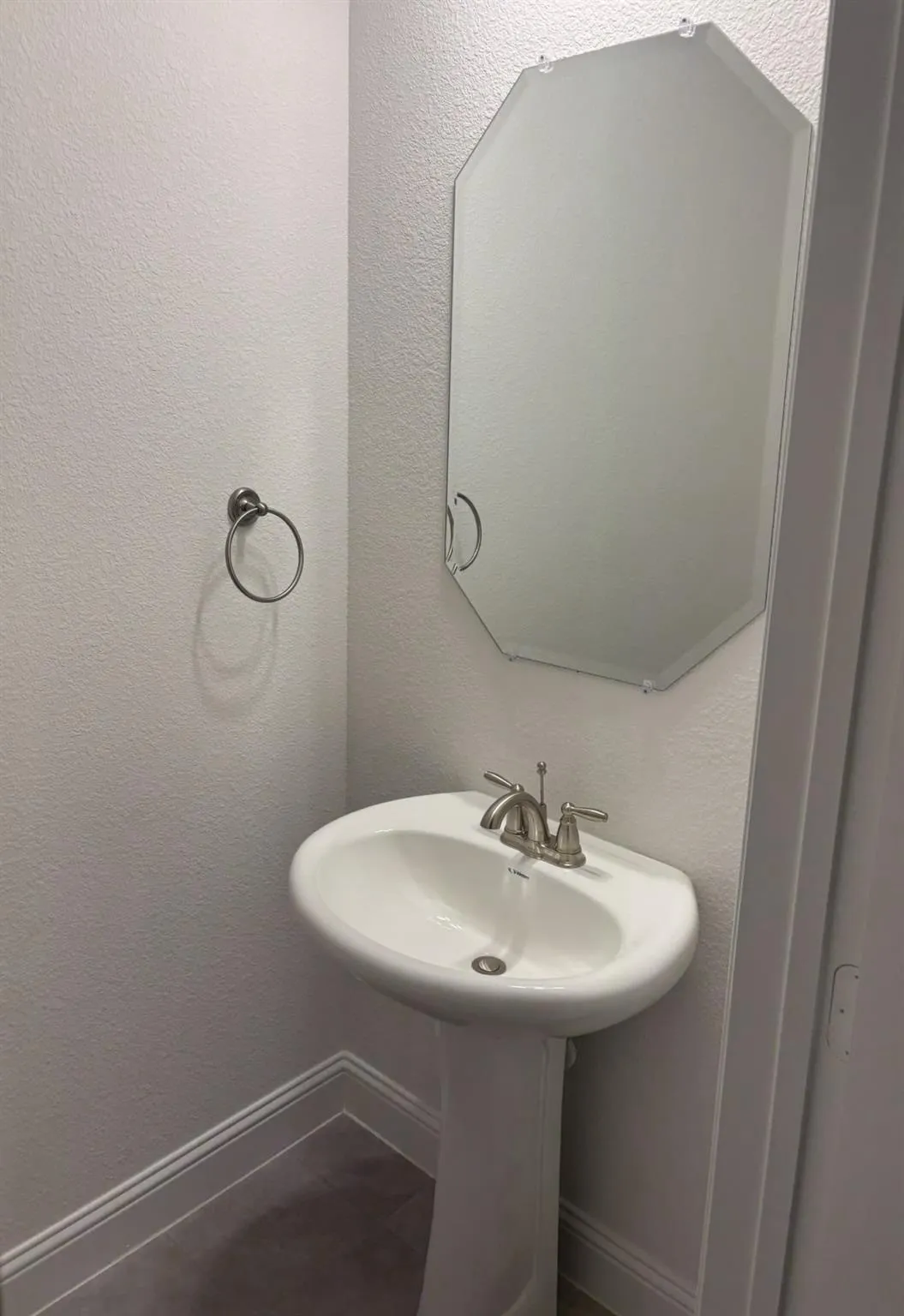 Pedestal sink with a polished chrome faucet, an octagonal mirror, and a wall-mounted towel ring