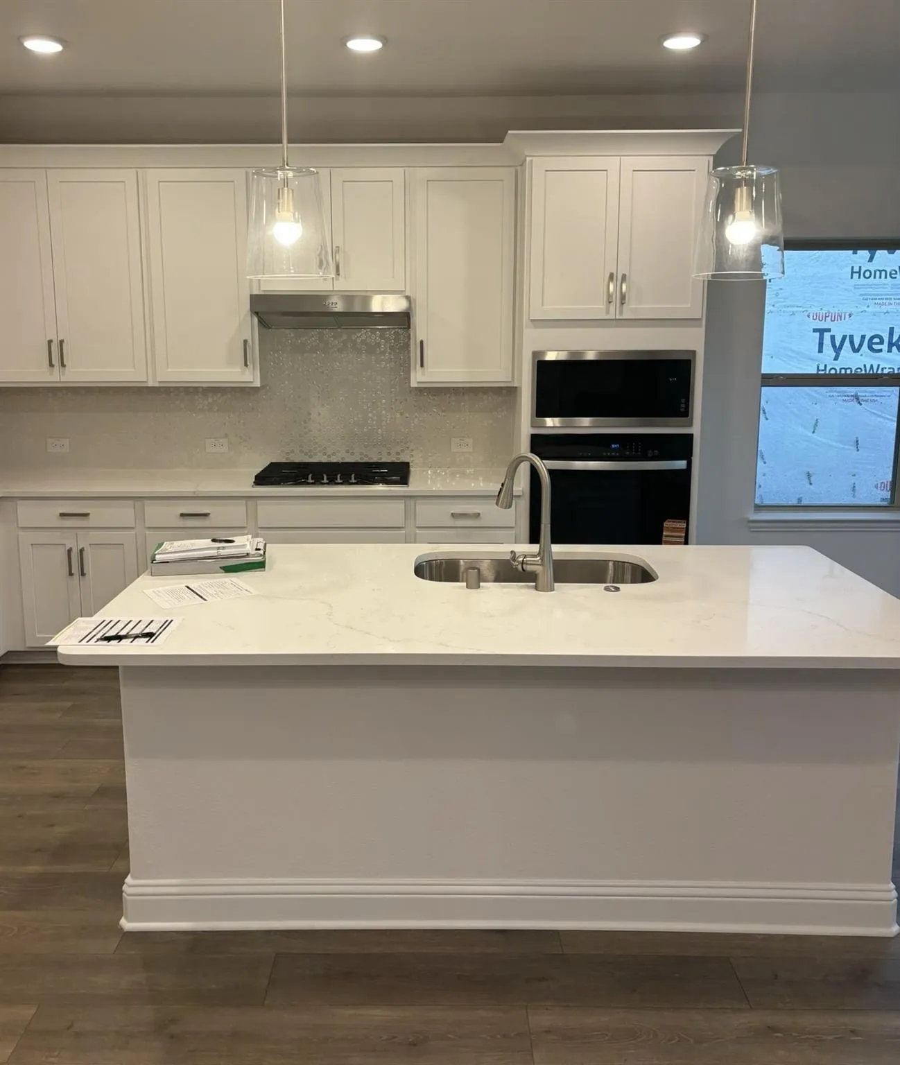 White shaker cabinetry, quartz countertops, stainless steel appliances, central kitchen island with undermount sink, and wood-finish flooring