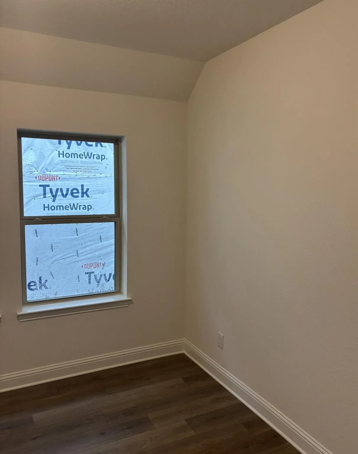 Wood-finish flooring with white trim, a single window, and neutral wall tones