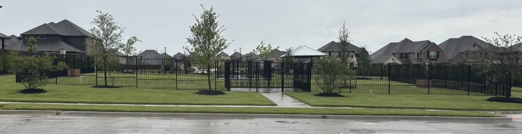 Expansive green space featuring a manicured lawn, established landscaping, and a secure wrought iron fence