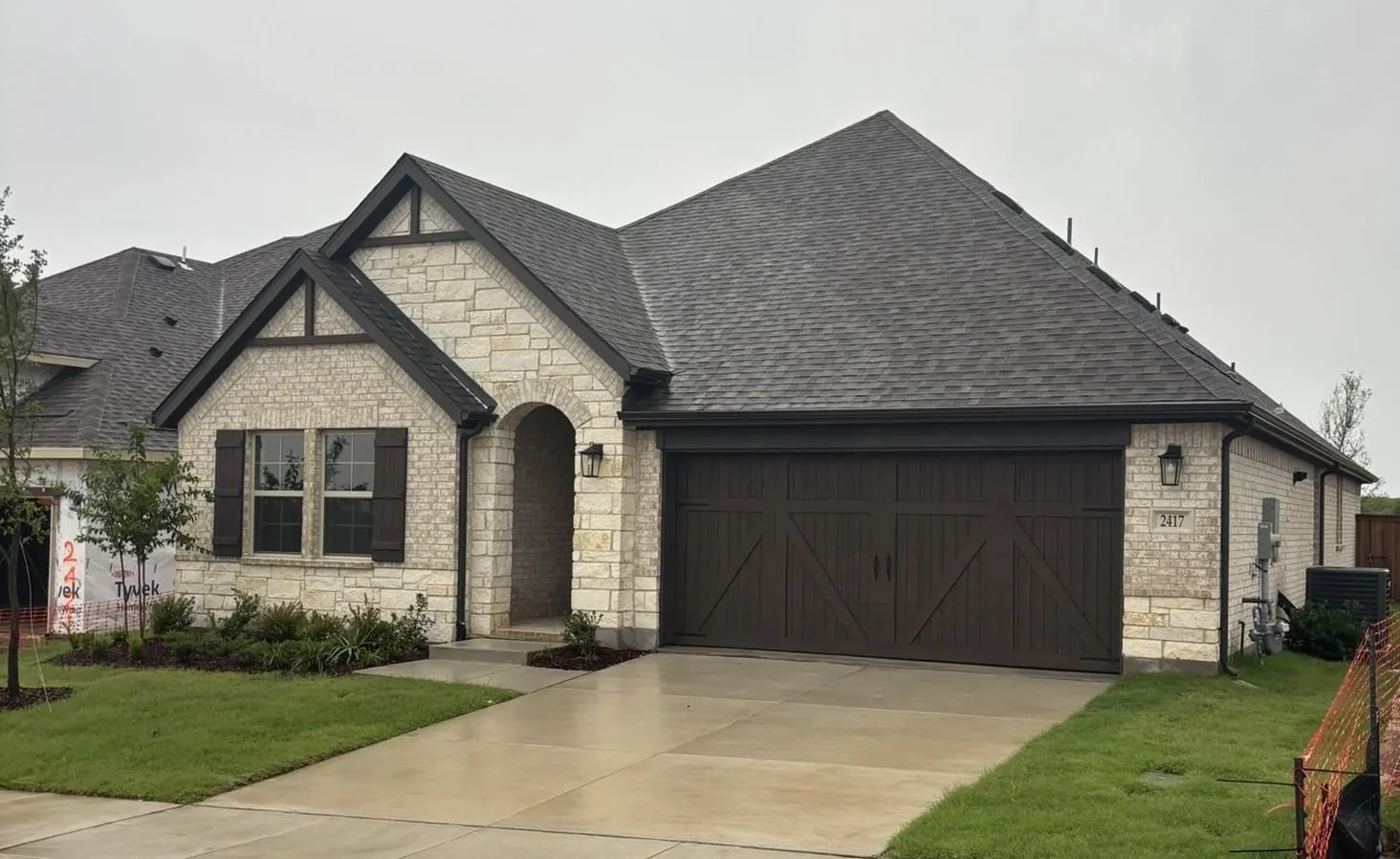 Stone facade with dark trim accents, arched entryway, dark wood-finish garage door, and a concrete driveway