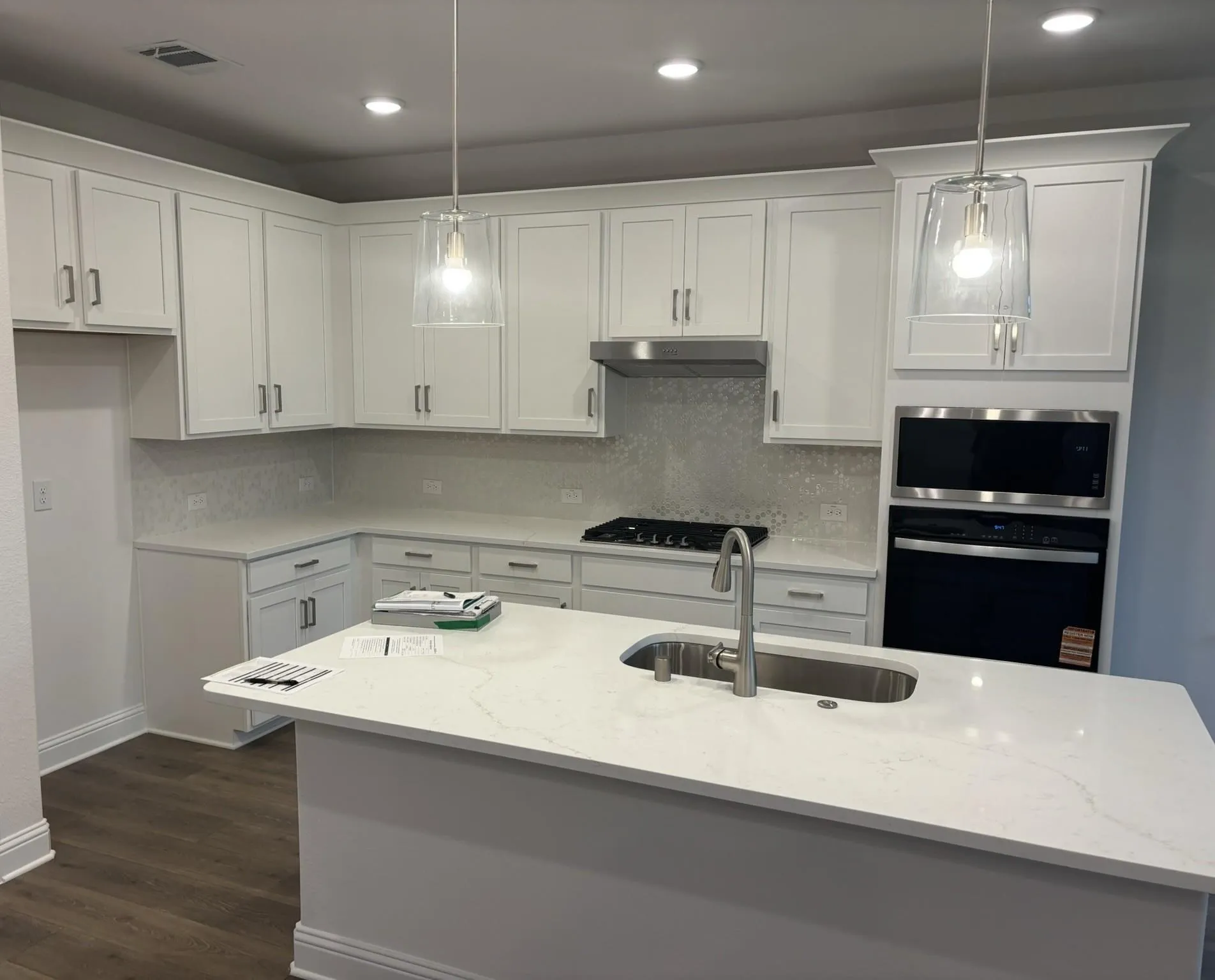 White shaker-style cabinetry with brushed nickel hardware, light-toned countertops, a stainless steel kitchen sink with a gooseneck faucet, an integrated oven and microwave, and wood-finish flooring