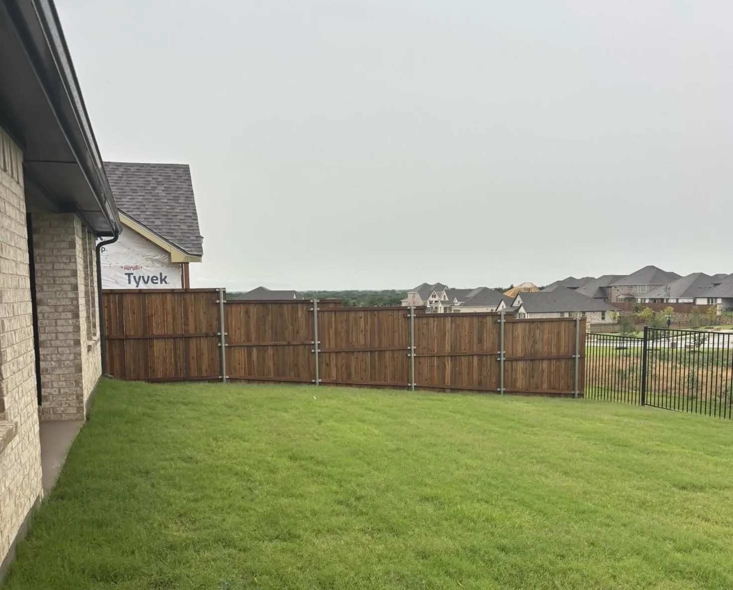 Expansive backyard with manicured lawn, full wood privacy fence, and additional black metal fencing