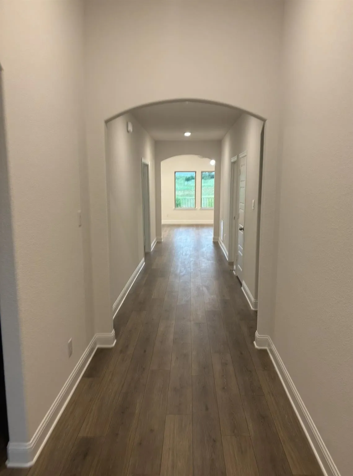 Archway entryway leading to a long hallway with wood-finish flooring