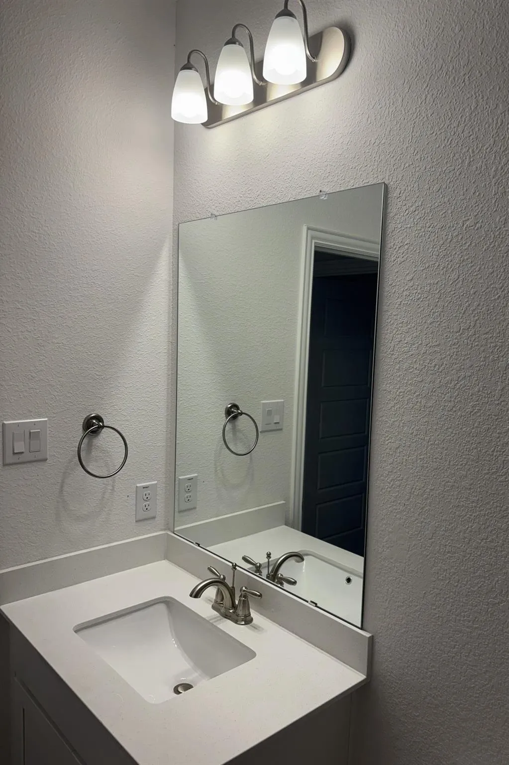 Vanity with an integrated rectangular sink, brushed nickel faucet, frameless mirror, and a three-light vanity fixture