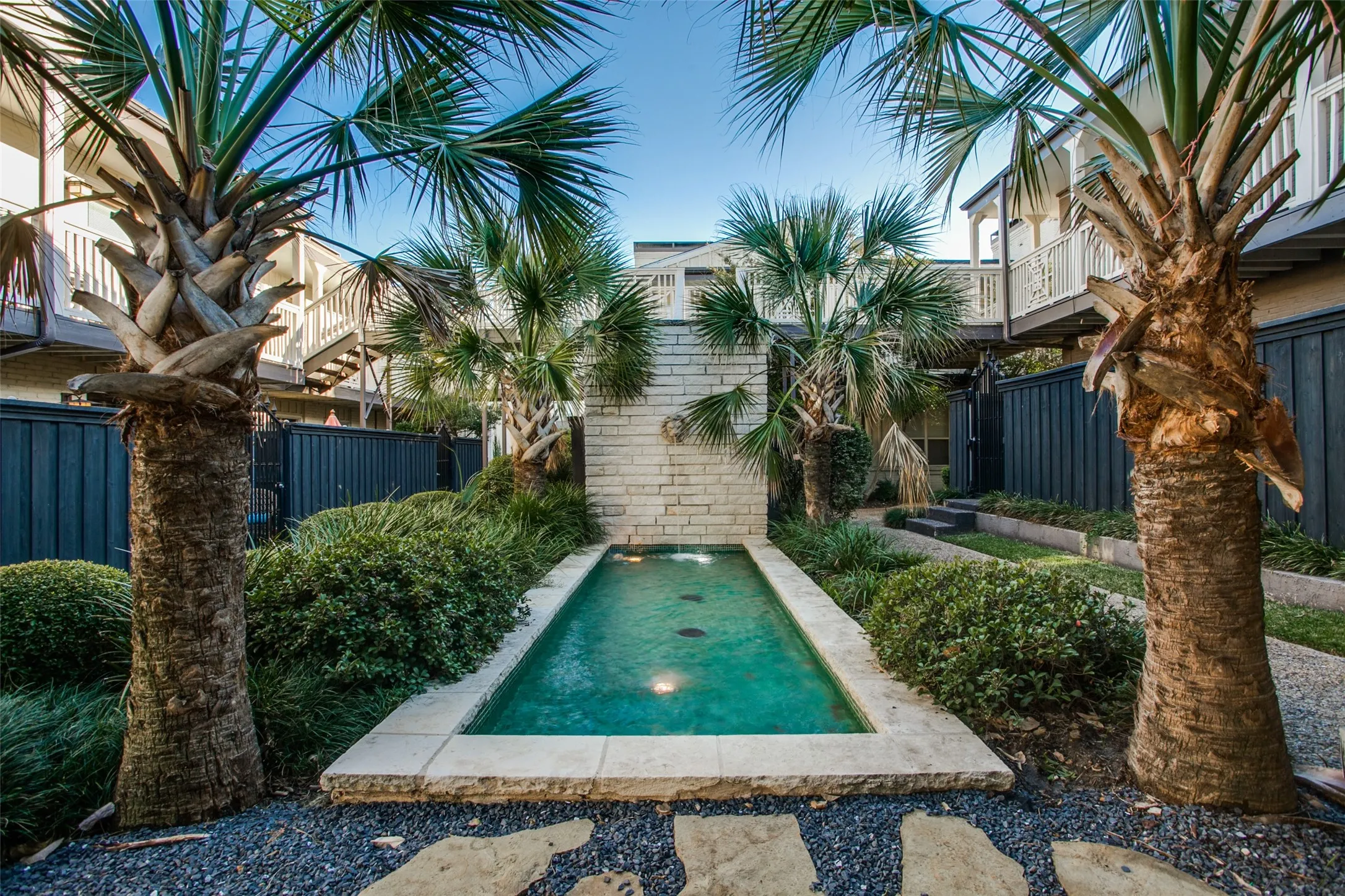 Landscaped courtyard featuring a rectangular water feature with a stone surround, stone accent wall, decorative gravel, and established palm trees