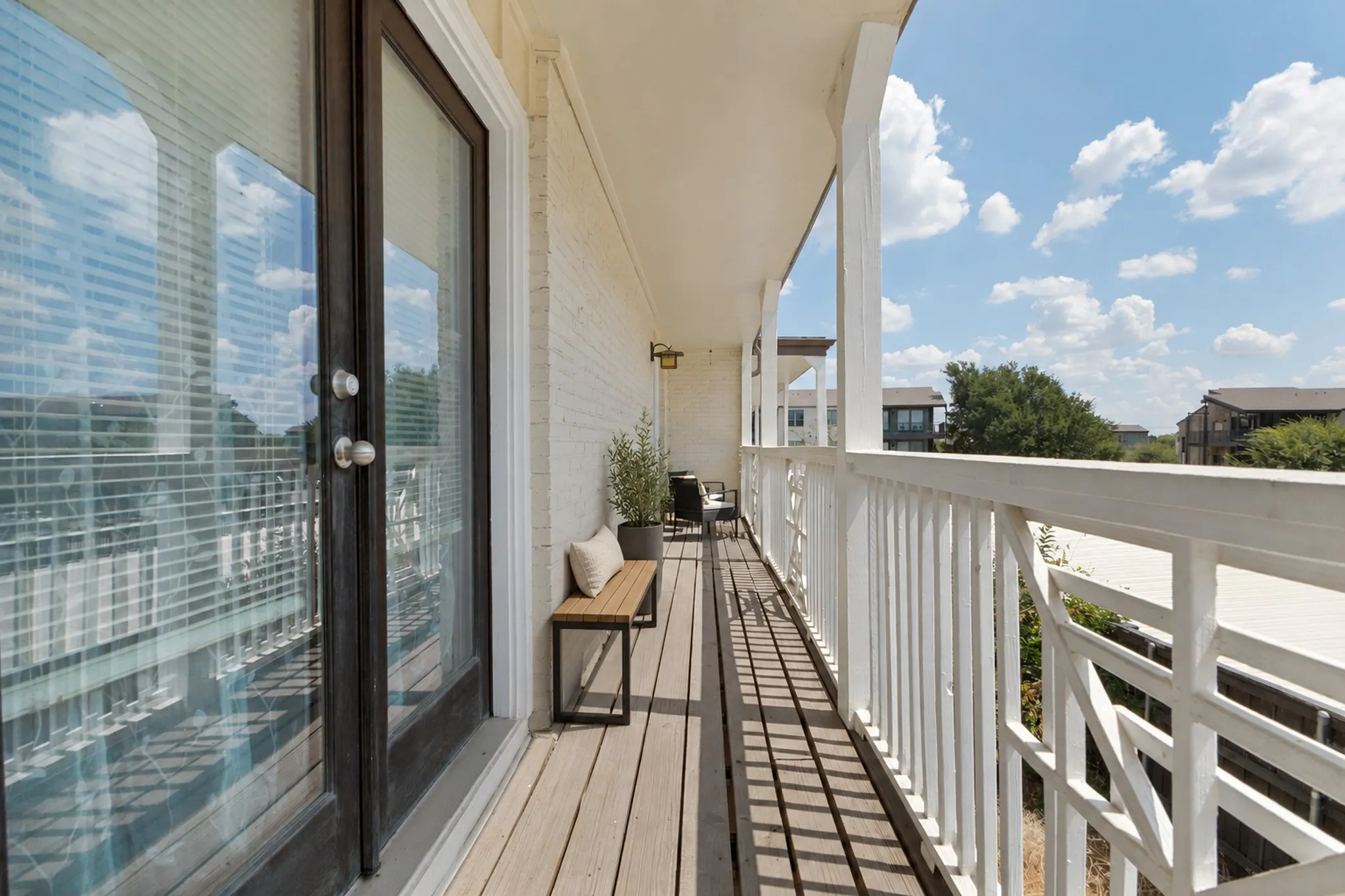 Private balcony with wood-finish decking, white painted brick exterior, and white architectural railings