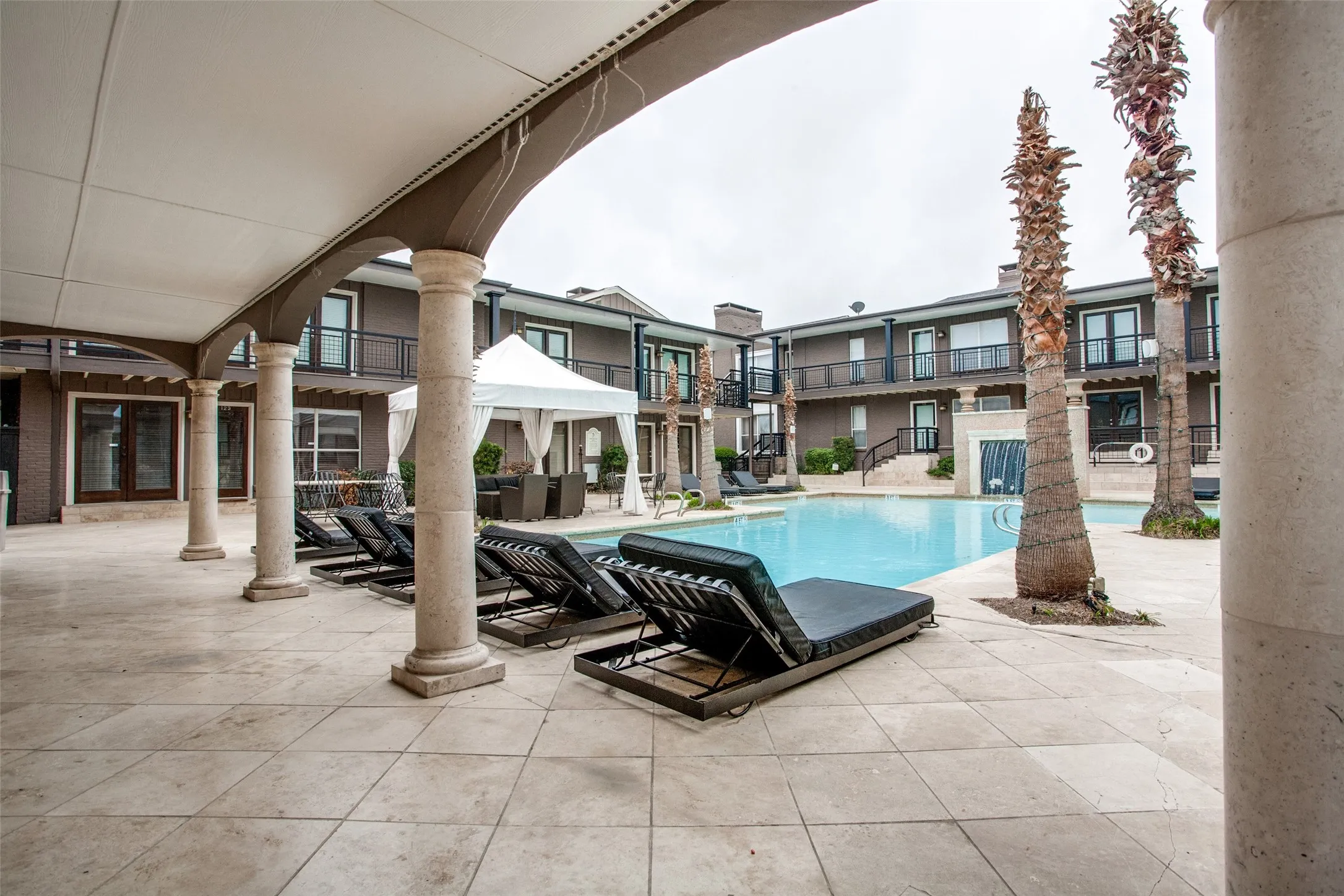 Expansive pool deck with tiled surfacing, arched covered patio, and column supports