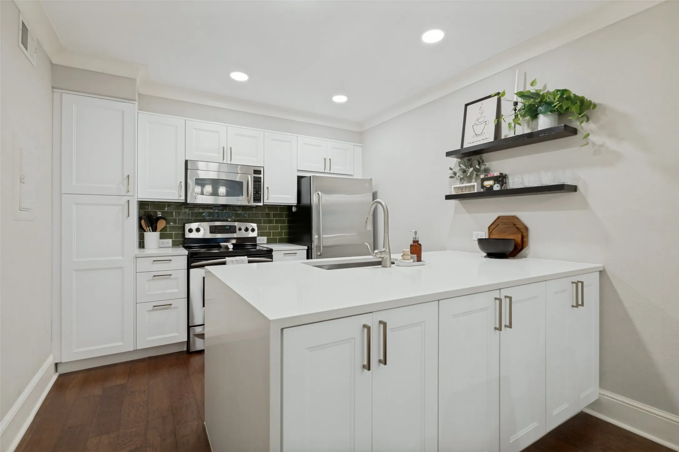 White shaker cabinetry paired with stainless steel appliances, a center island featuring an undermount sink, recessed lighting, and wood-finish flooring
