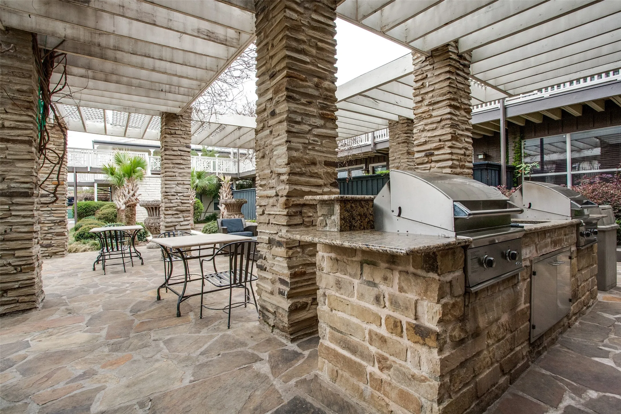Outdoor entertainment area featuring a stone patio, stone-clad columns, a pergola, and a built-in barbecue station with stainless steel grills and granite-look countertops