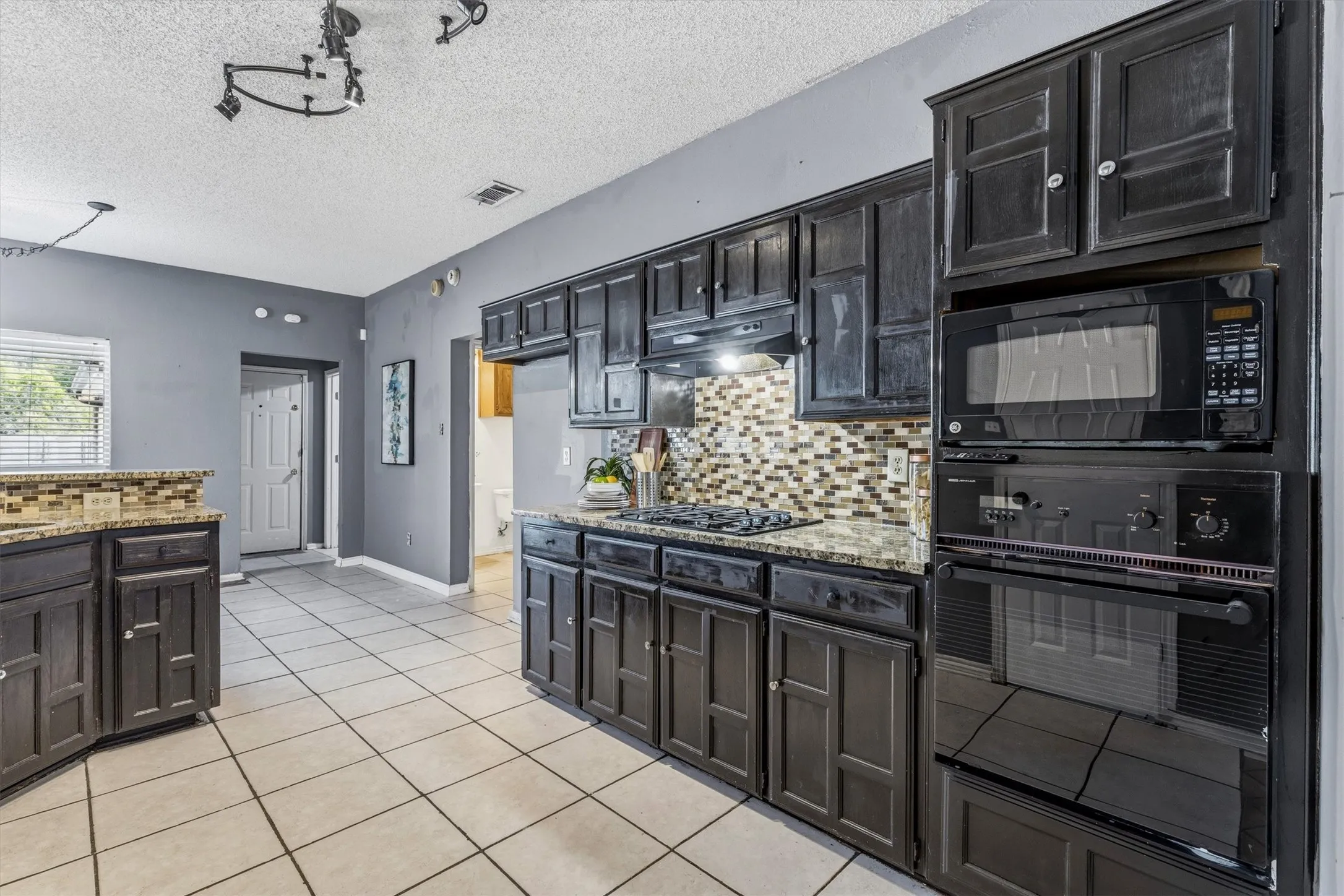 Chef's kitchen featuring dark cabinetry with glass-front upper cabinets, stainless steel dual wall ovens, built-in microwave, mosaic tile backsplash, and granite countertops