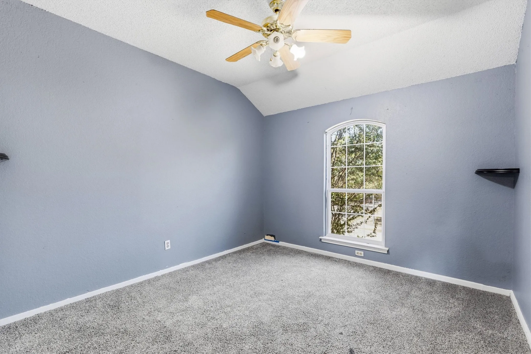 Vaulted ceiling with a ceiling fan, arched window, and wall-to-wall carpeting