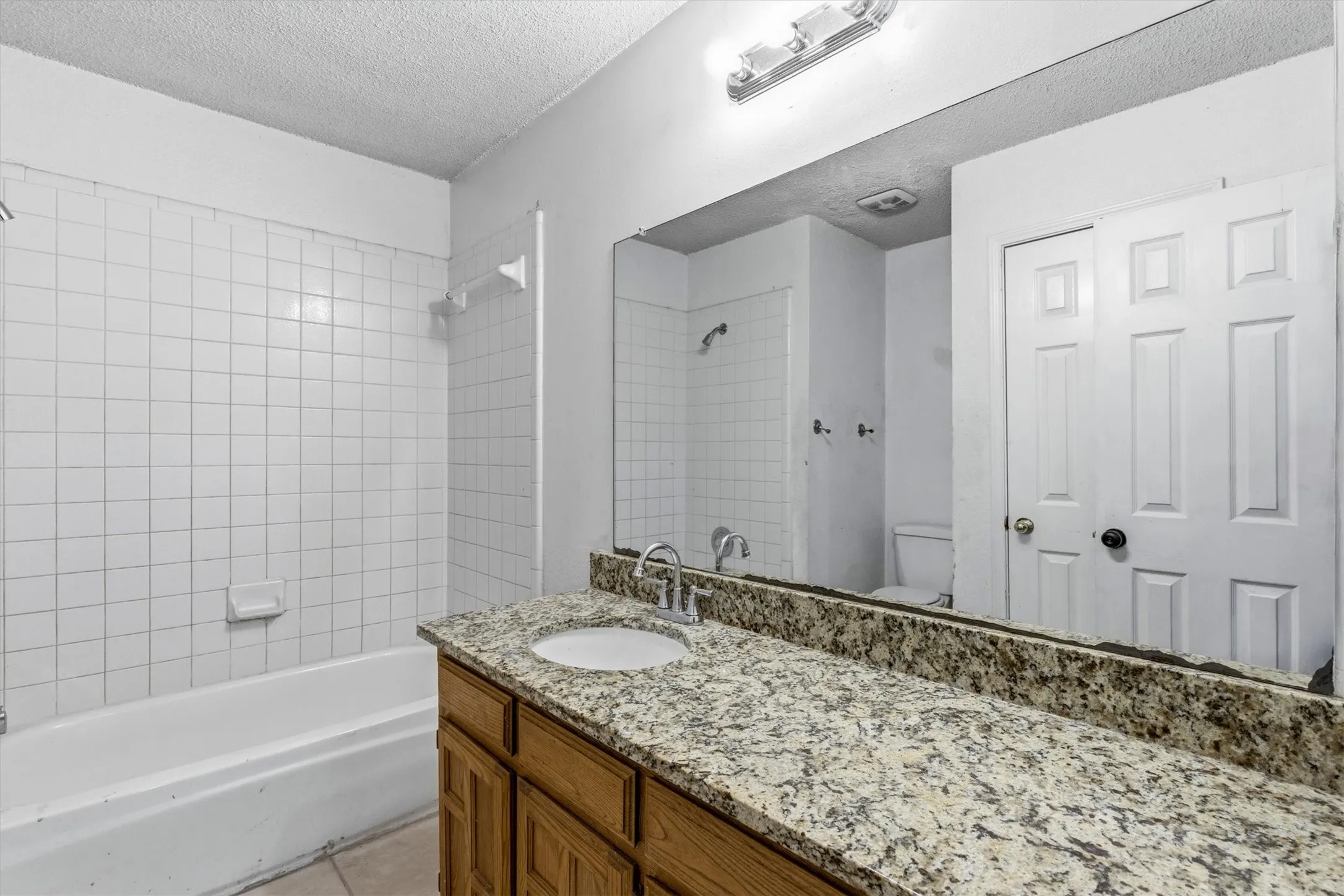 Bathroom featuring a vanity with a drop-in sink, stone countertop, wood-finish cabinetry, and a full-width mirror