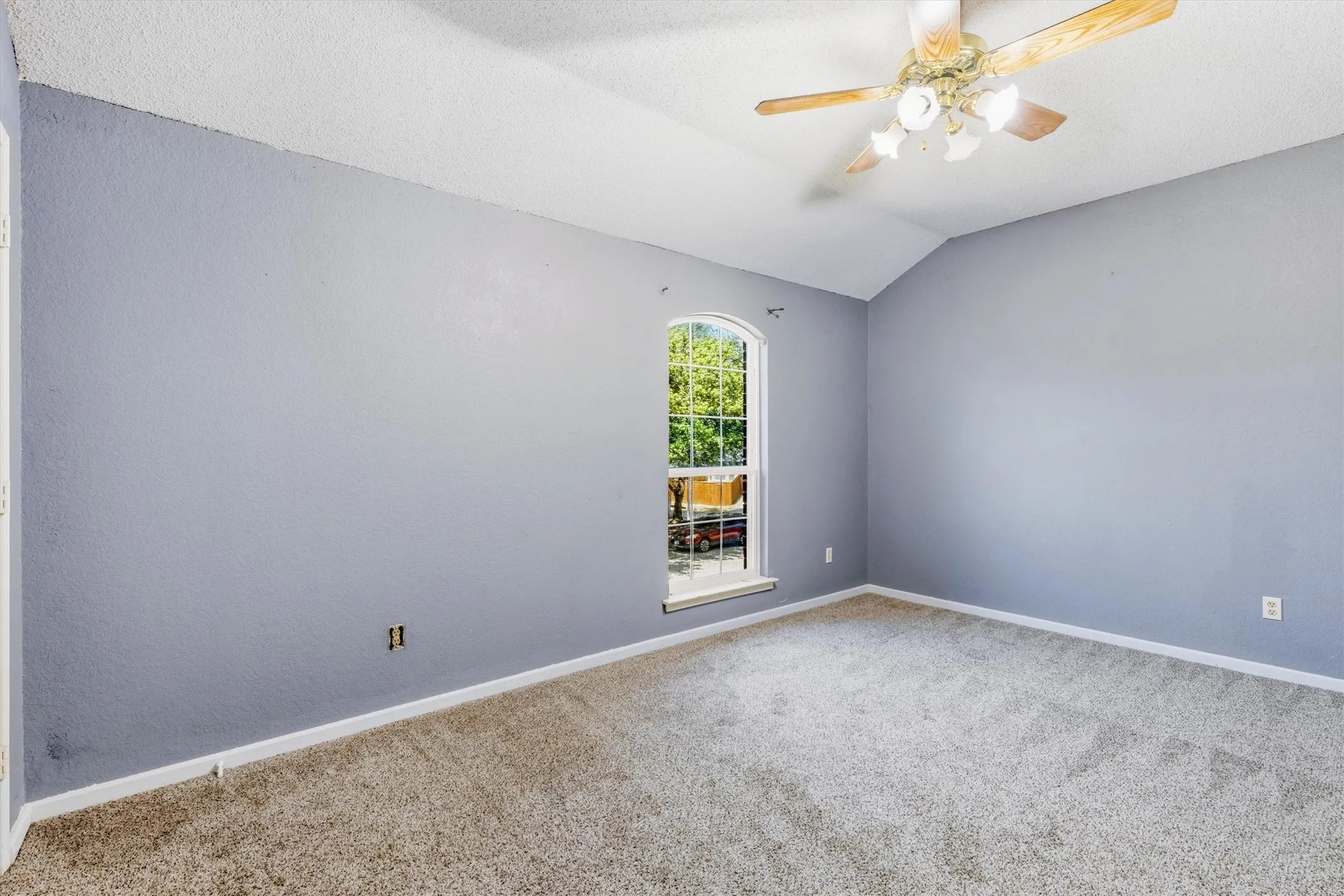 Vaulted ceiling with a wood-finish ceiling fan, arched window, and textured carpeting