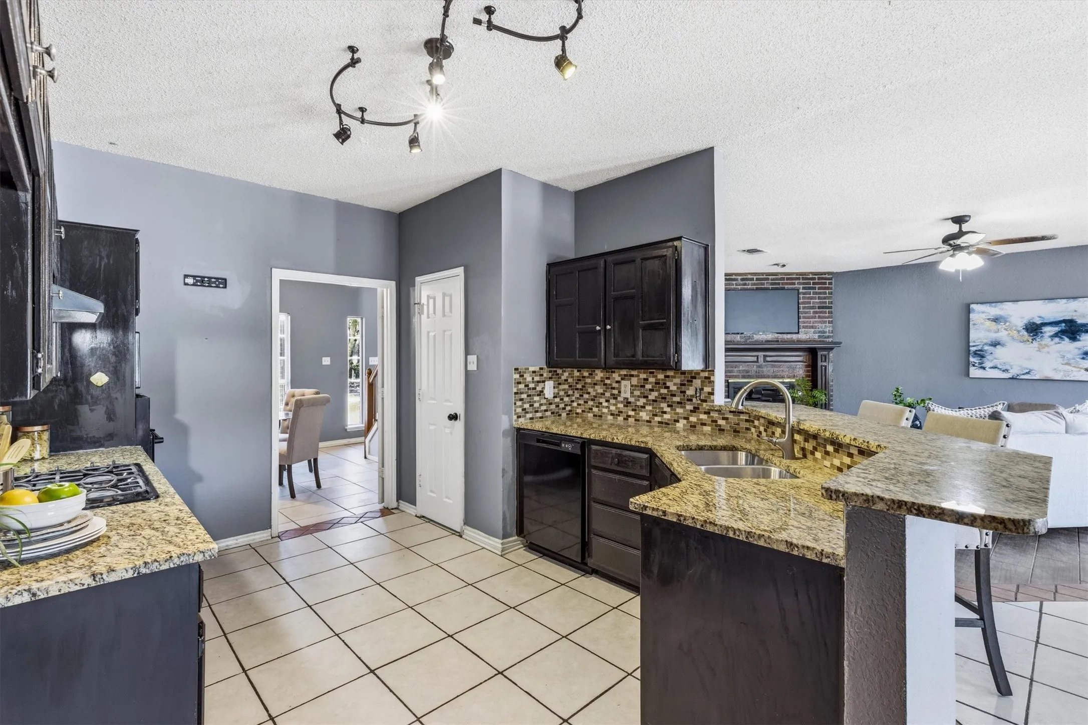 Kitchen featuring granite-style countertops, tile flooring, dark wood-finish cabinetry, a dual basin sink, and a tile backsplash