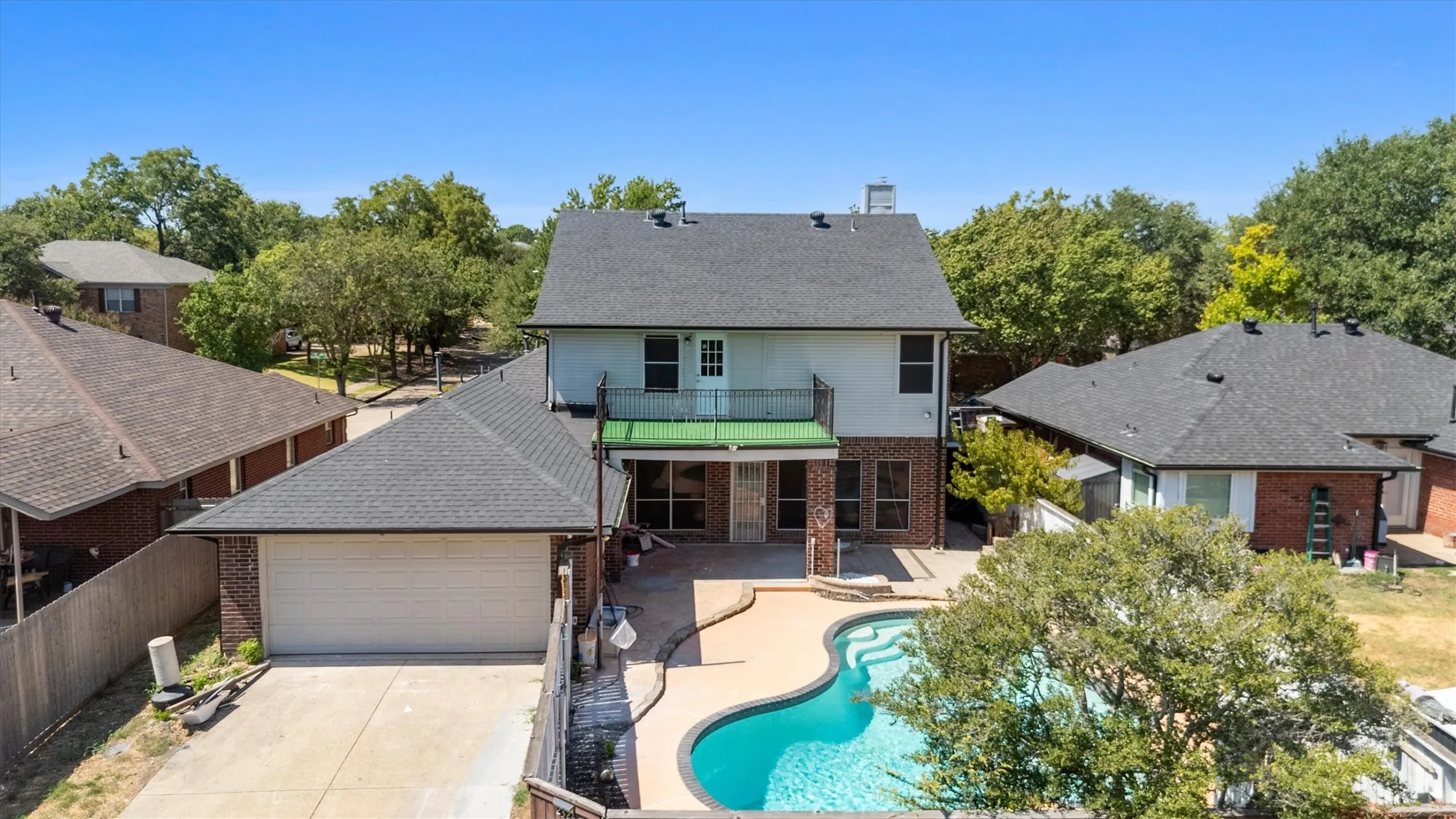 Rear exterior with a concrete patio, a built-in swimming pool, a two-story structure with a second-level balcony, and an attached two-car garage